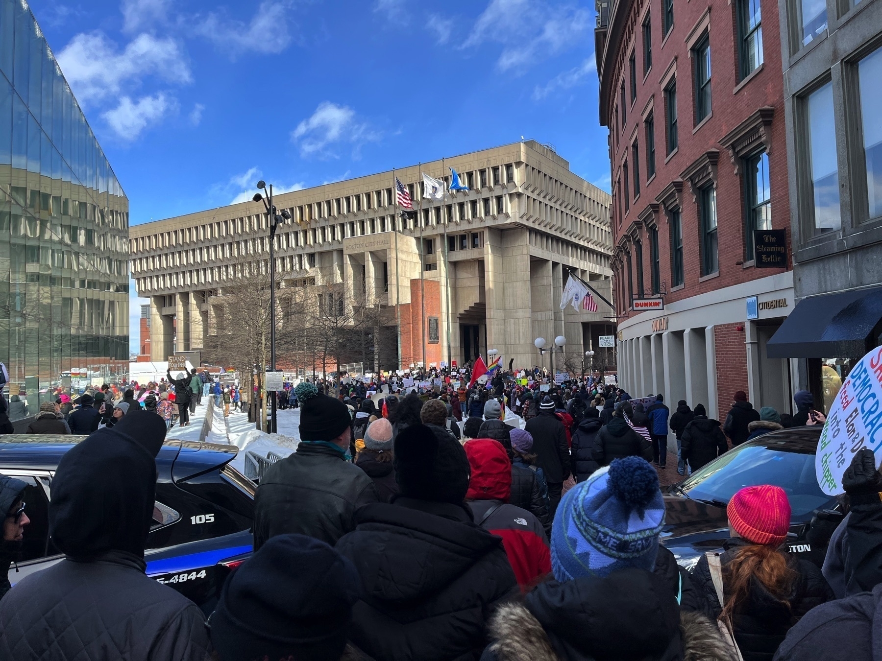 This picture is in front of Boston City Hall. There is a big crowd of people.