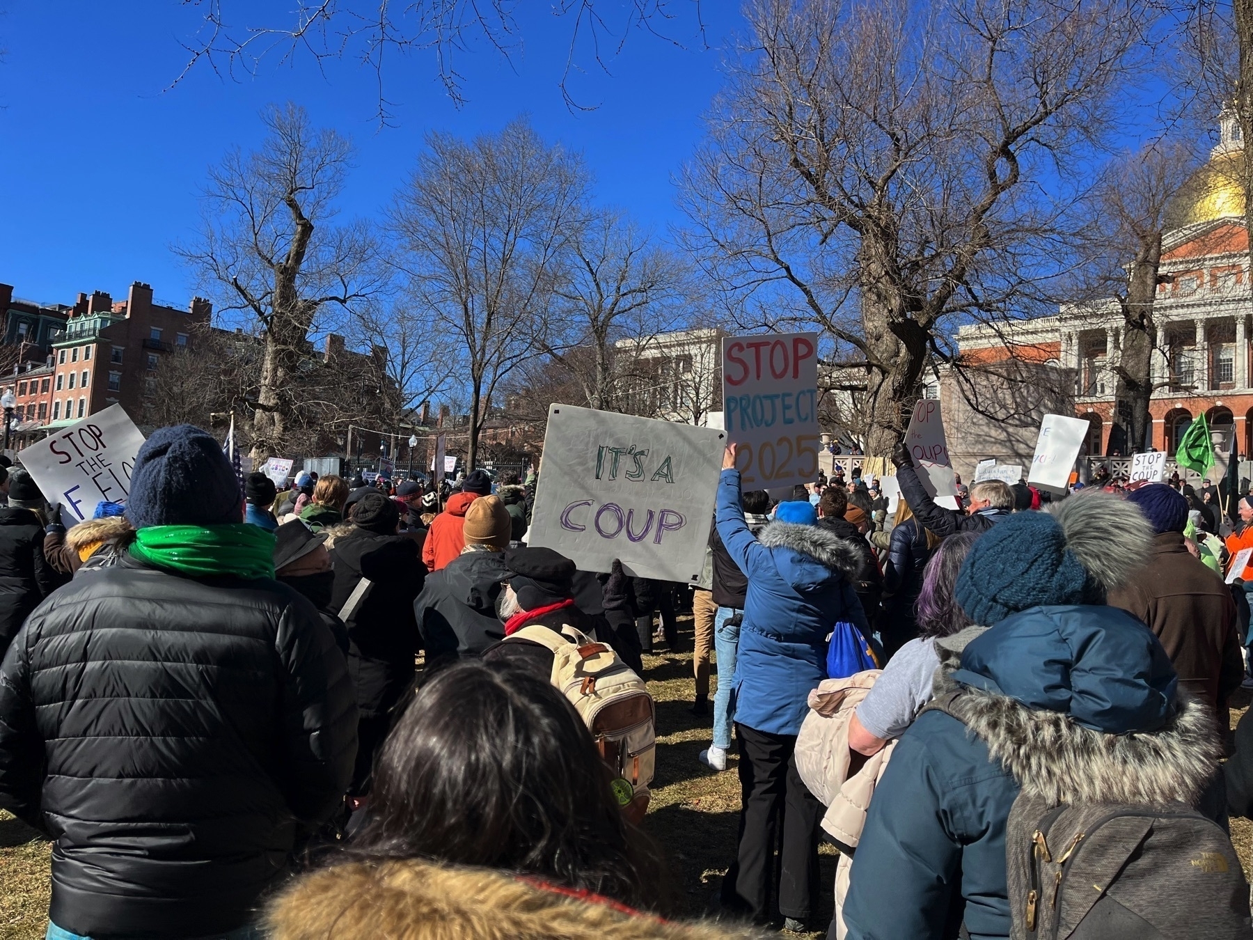 Lots of people with signs. One says ”stop project 2025”. Anther says ”it’s a coup”.