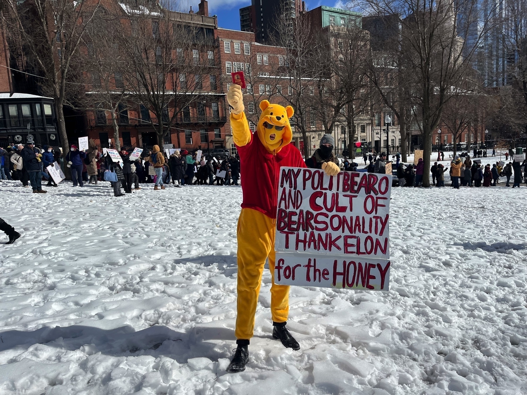 A person with a Winnie the Pooh costume is holding a sign reading ”my politbearo and cult of bearsonality thank elon for the honey”.