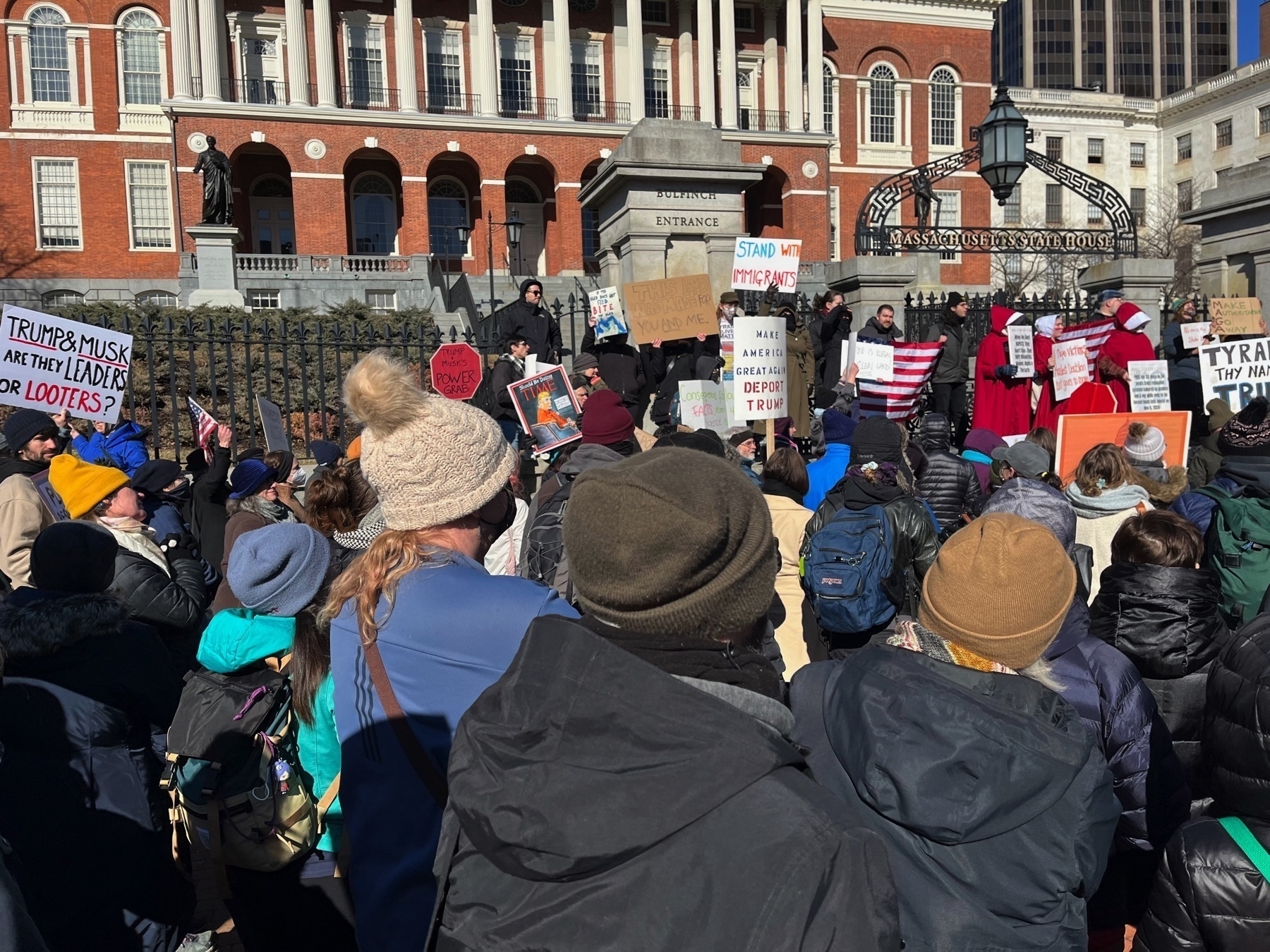 One sign says “Trump & Musk - are they leaders or looters?”. One says “Trump & Musk power grab”. One says “stand with immigrants” One says “make America great again - deport Trump”. One says “tyranny, thy name is Trump”.