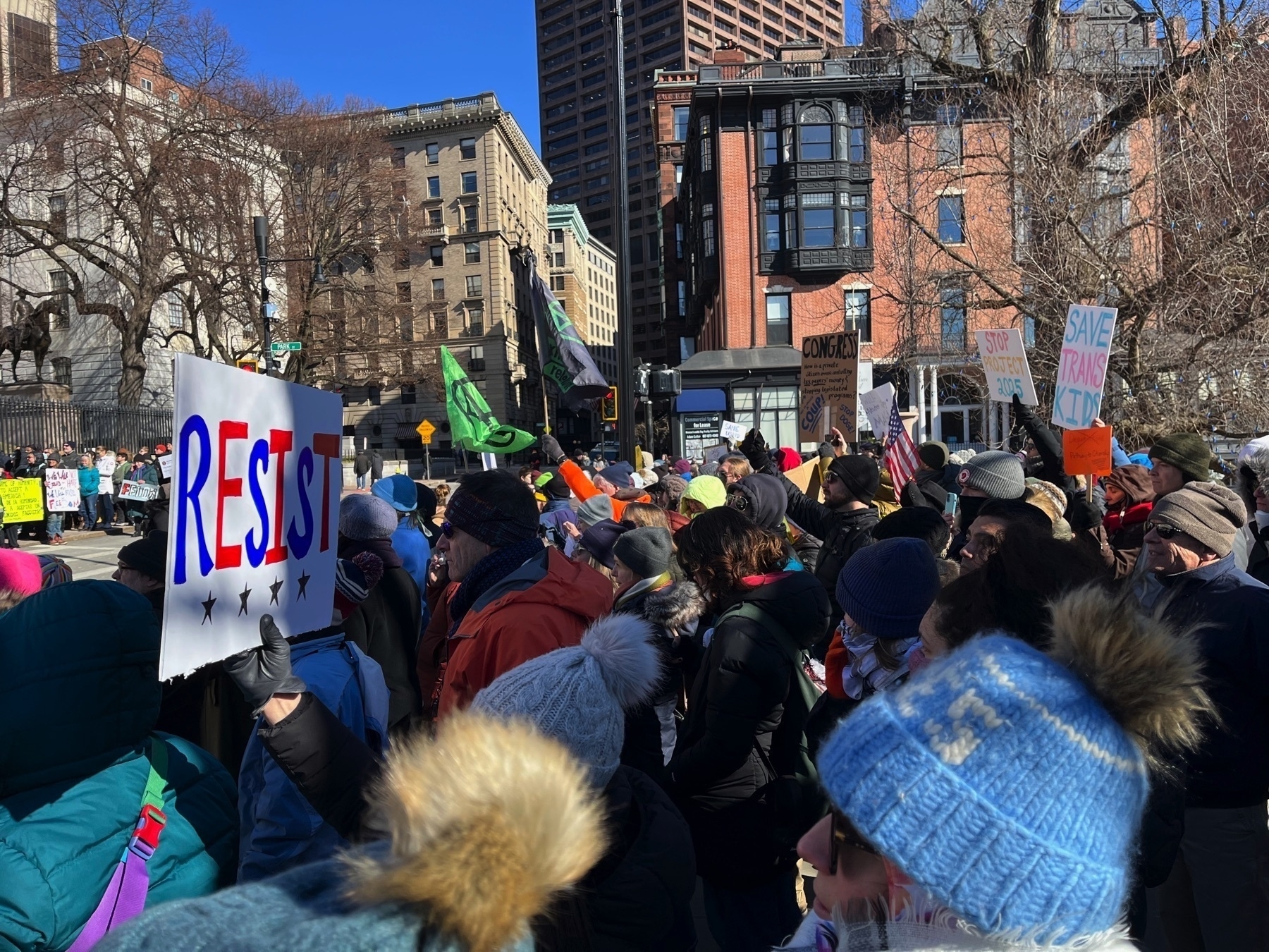 Lots of folks with sign. One says ”stop project 2025”. One says ”save trans kids”. One says “resist”.