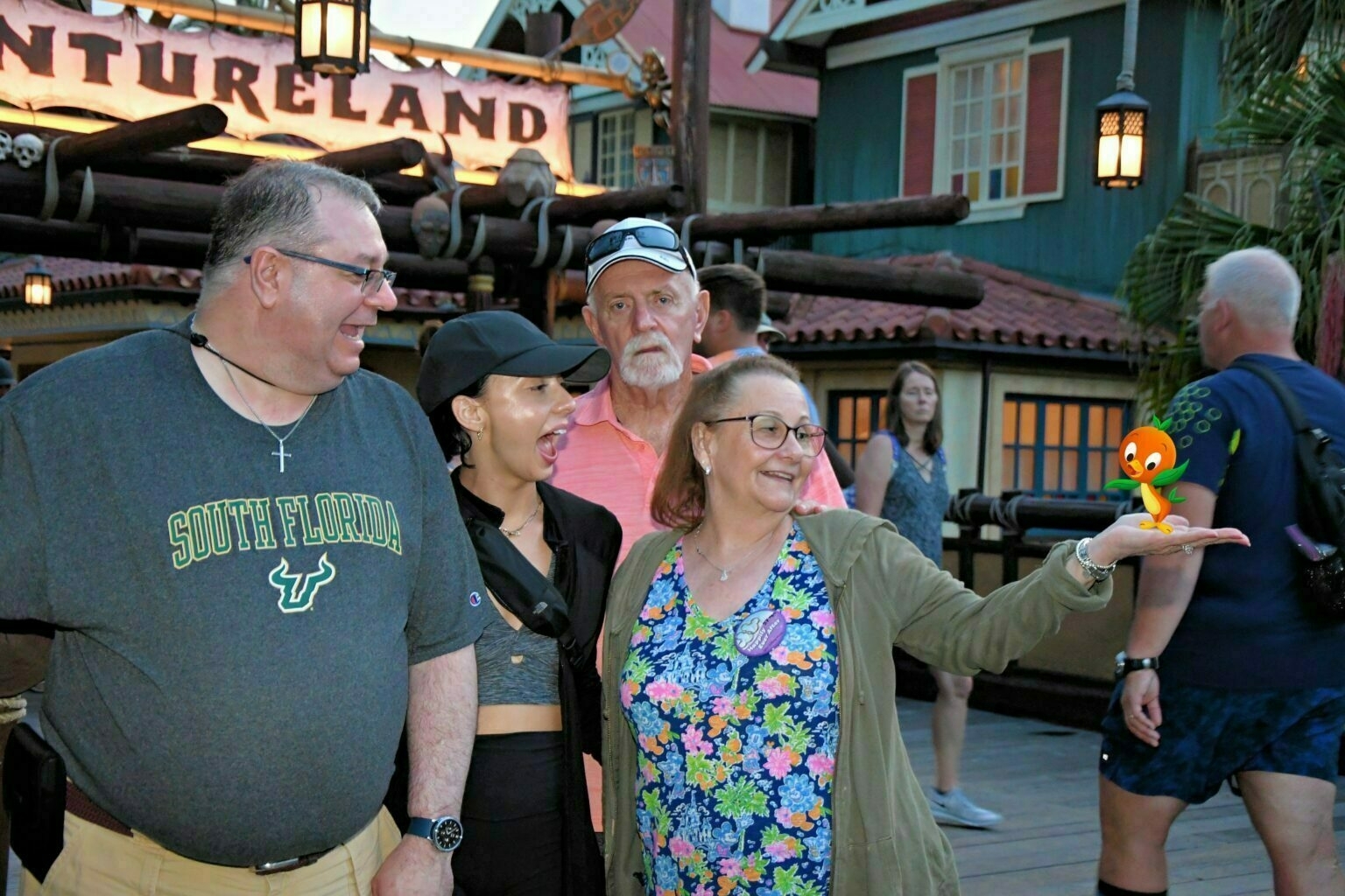 A group of people is standing in front of Adventureland, with a small colorful figure perched on a woman's hand.