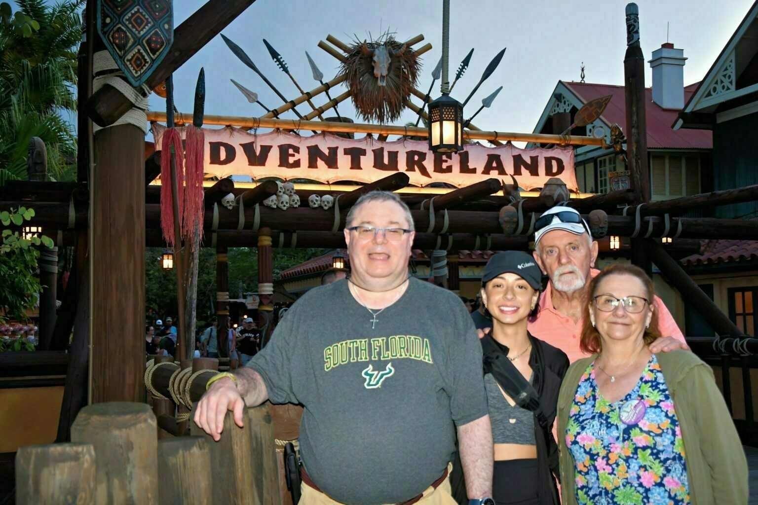 A group of four people posing in front of the Adventureland entrance at a theme park.