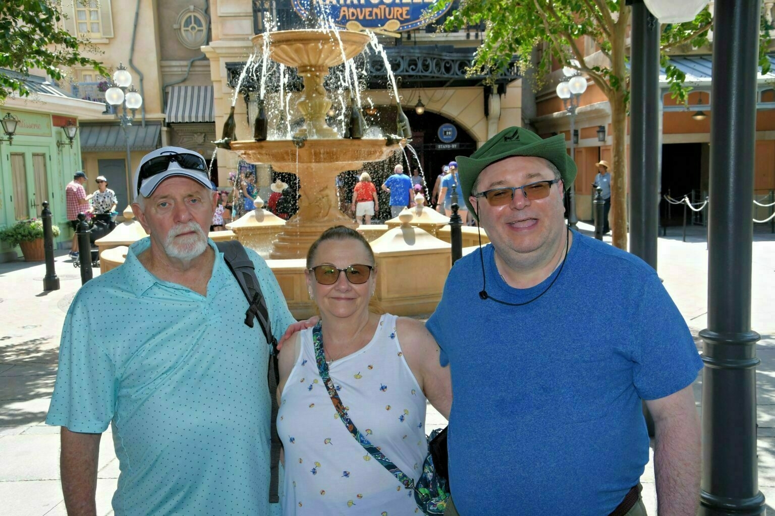 Three people are posing for a photo in front of a large fountain at an amusement park.