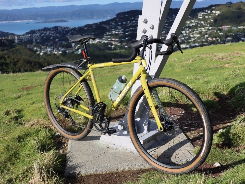 A yellow road bike with fat tyres leaning against a power pylon on a hill above a city