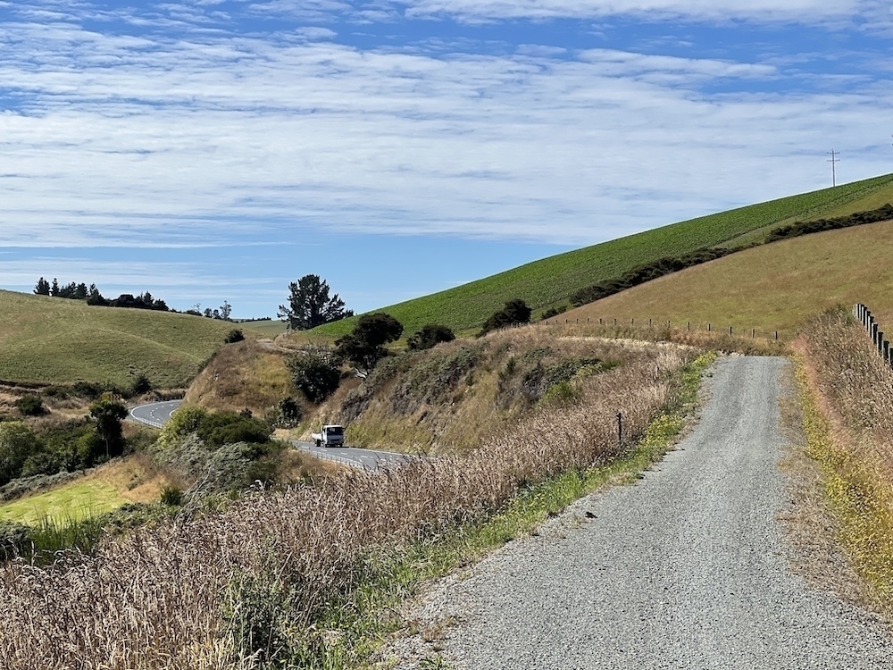 The trail winds across green pastured hills above a highway