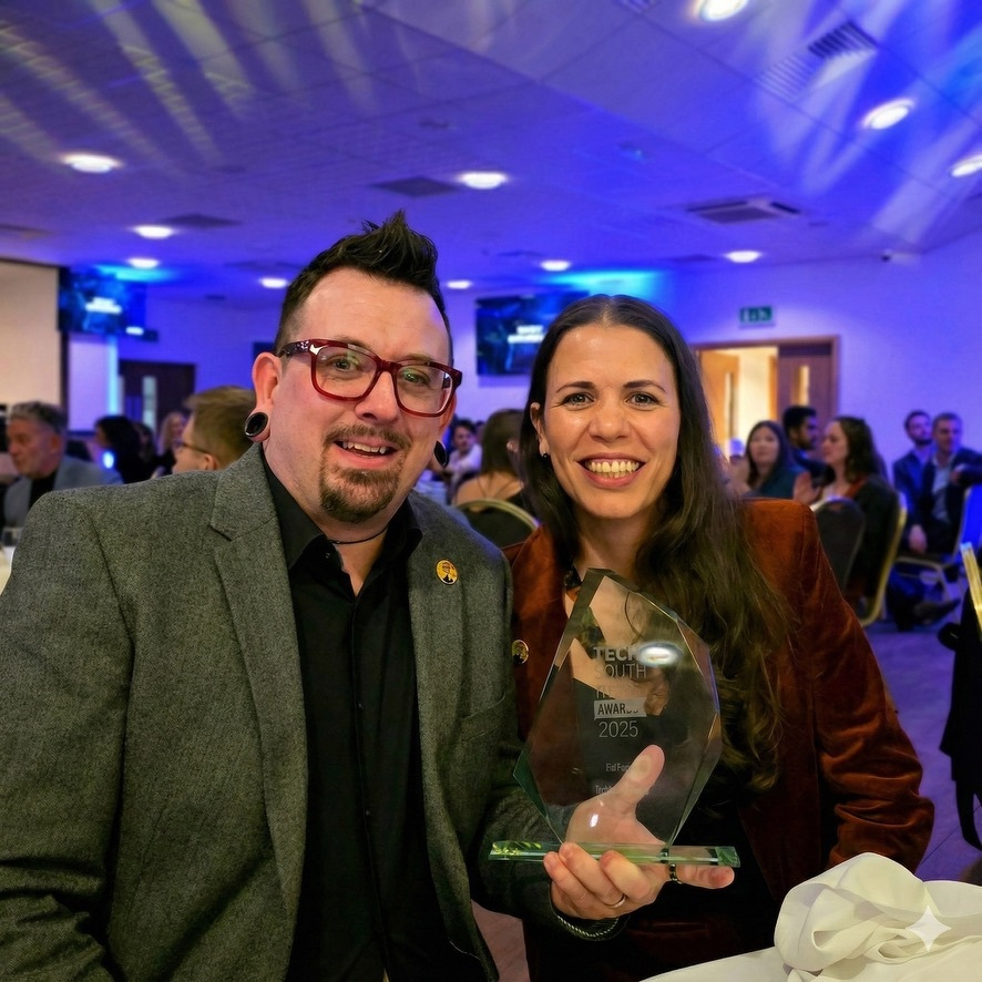 Auto-generated description: A man and a woman are sitting together at an event, with the woman holding a glass award.