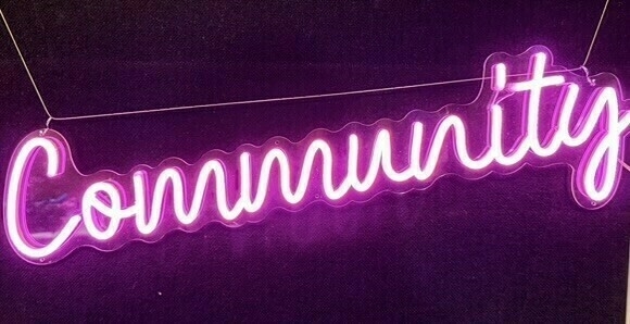 Auto-generated description: A neon sign displays the word Community in vibrant pink letters against a dark background.