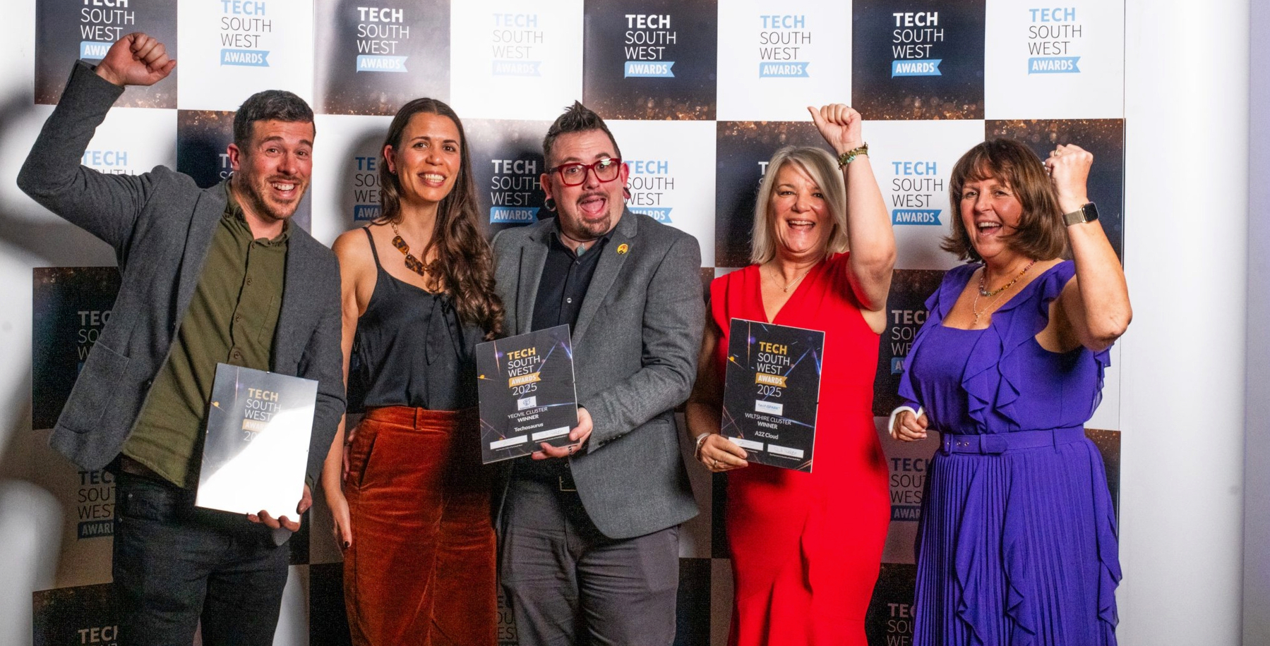 Auto-generated description: A group of five people is celebrating while holding awards in front of a Tech South West Awards backdrop.