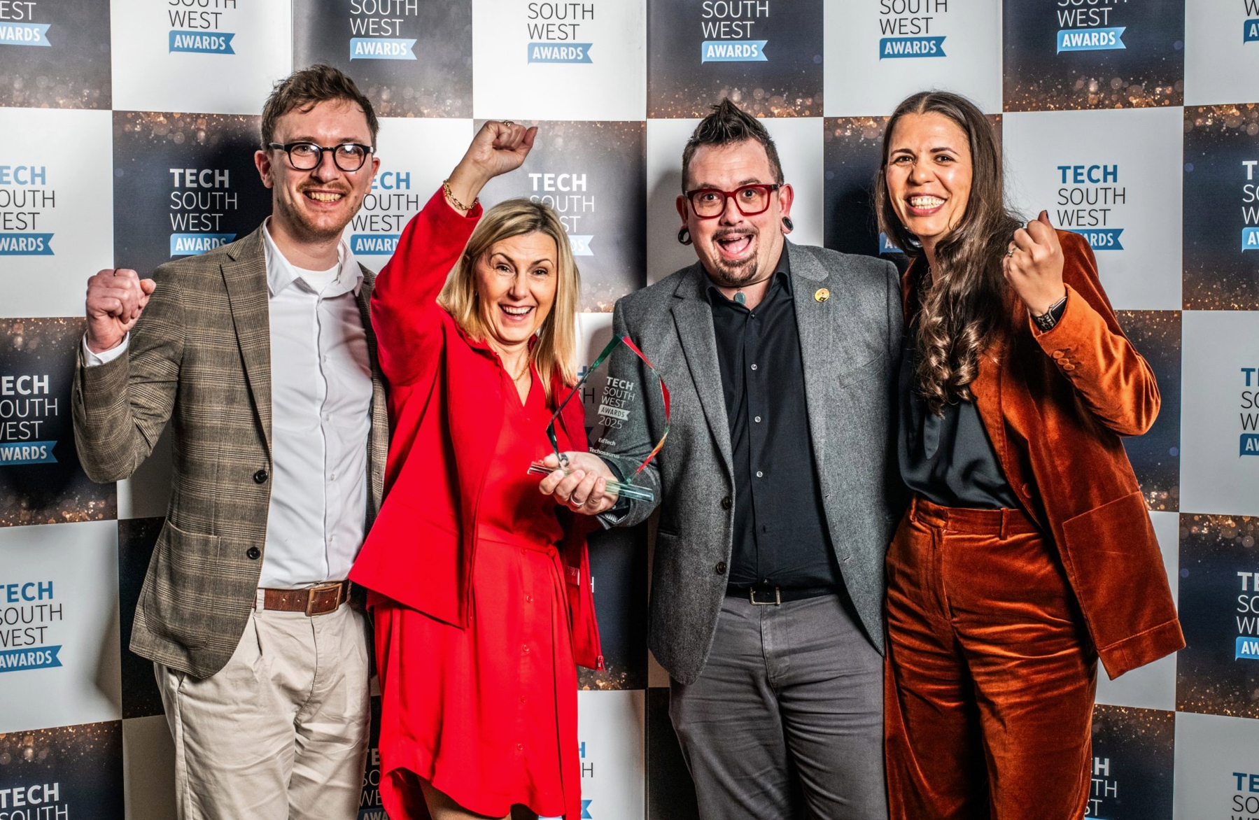 Auto-generated description: Four people are celebrating and holding a trophy at the Tech South West Awards.