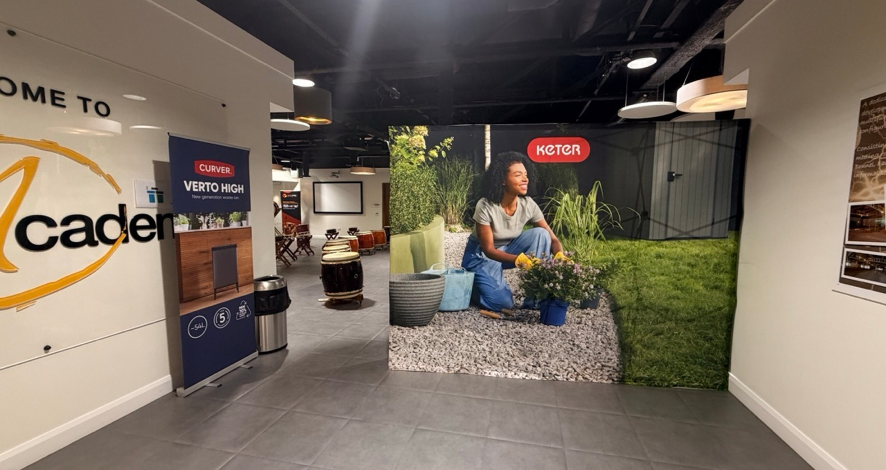 Auto-generated description: A store display features gardening products with a life-size image of a person holding a plant pot, surrounded by various containers, against a backdrop of greenery.