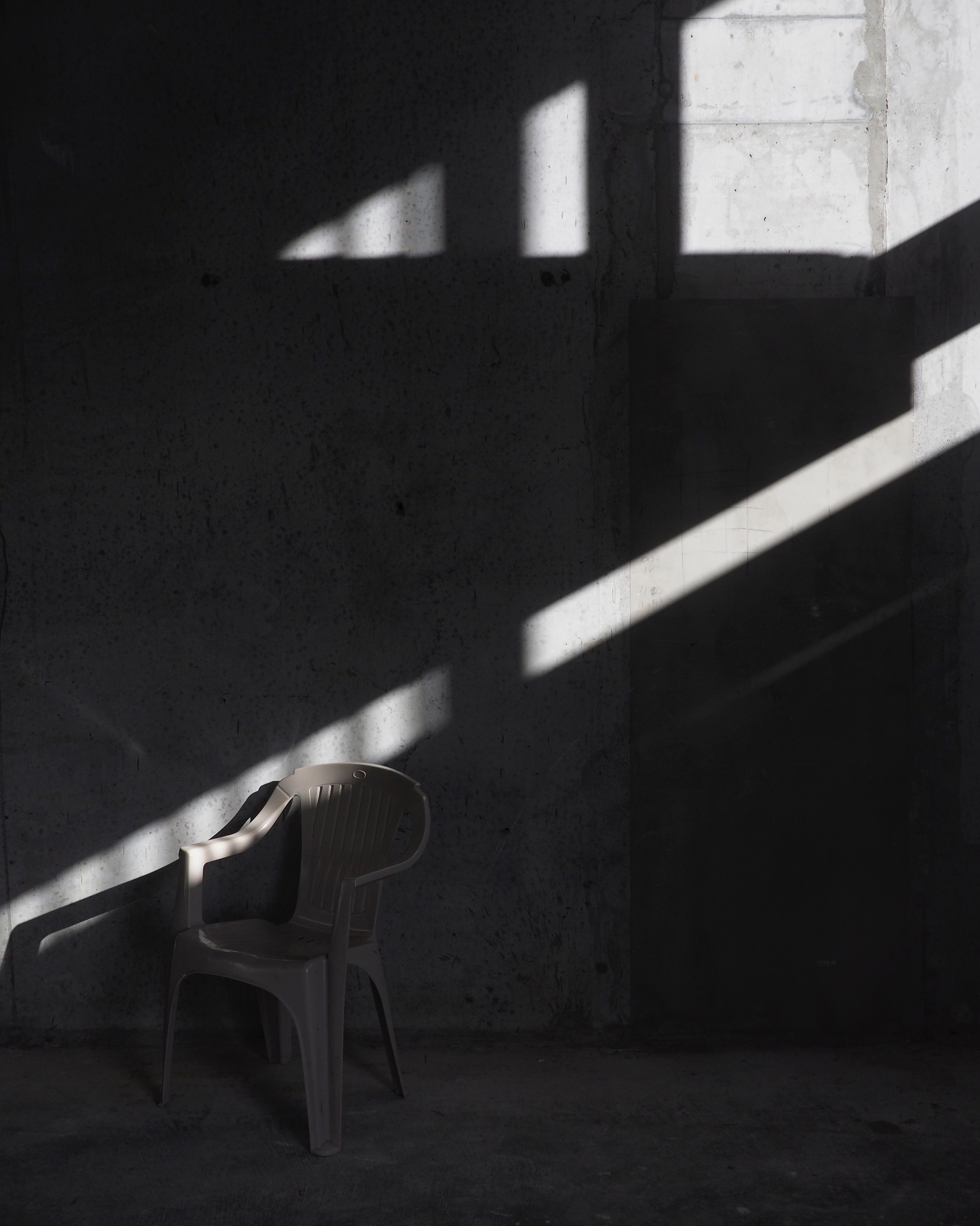 A shaft of light cutting across a plastic chair in a dim concrete room.