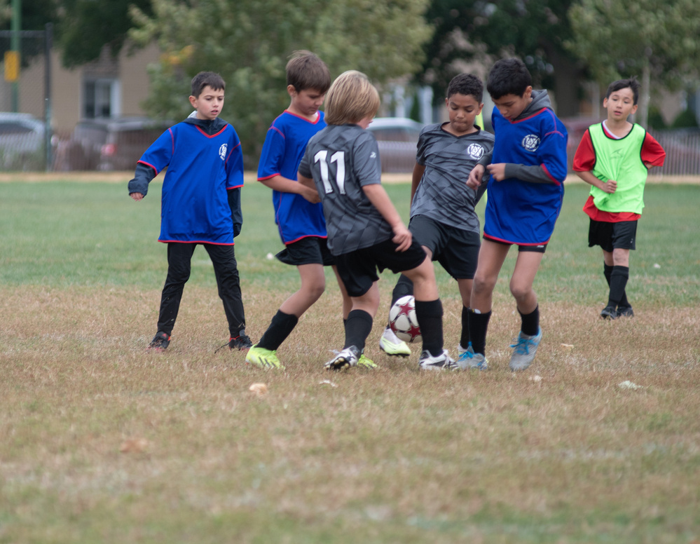 A group of kids is playing soccer on a grassy field, with two players actively contesting for the ball while others look on.