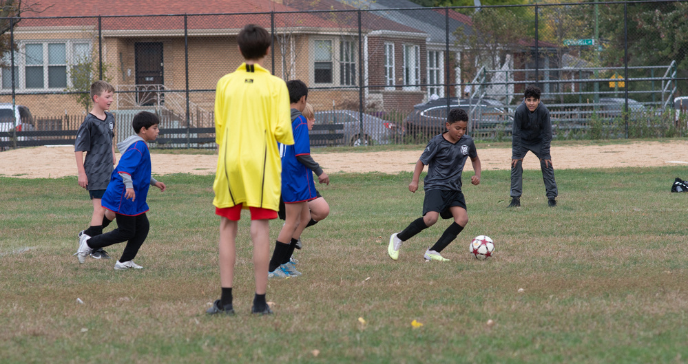 A group of children are playing soccer on a grassy field, with one child dribbling the ball.