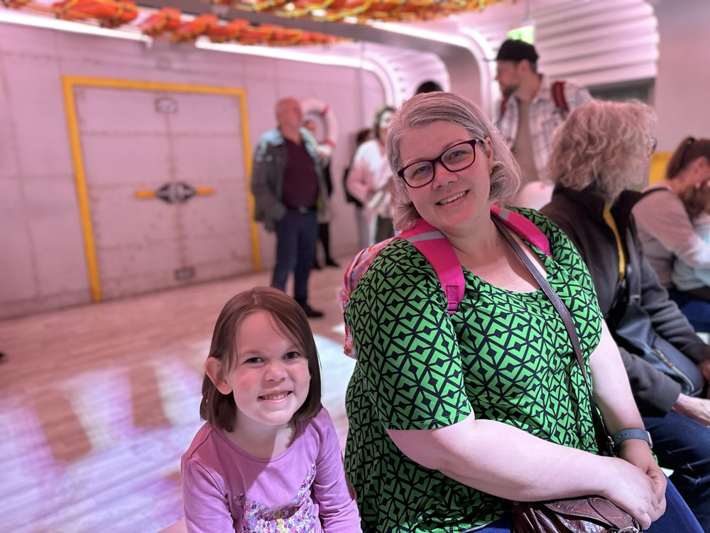 Mother and daughter smiling at the camera while sitting in an exhibit room simulating a boat ride to Jurassic World.