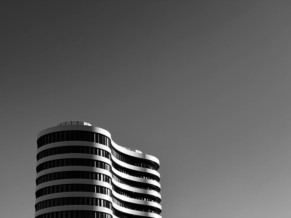 Black and white photo of an office building tower, with unique curved architecture, on the left side. 