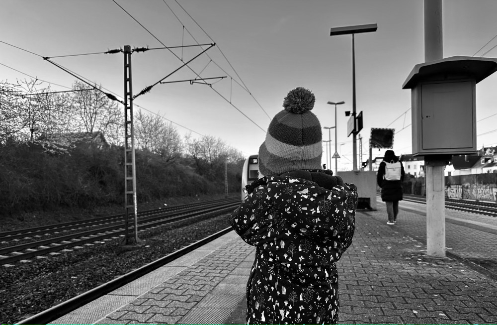 Little girl standing on brick platform waiting on a train that is arriving.