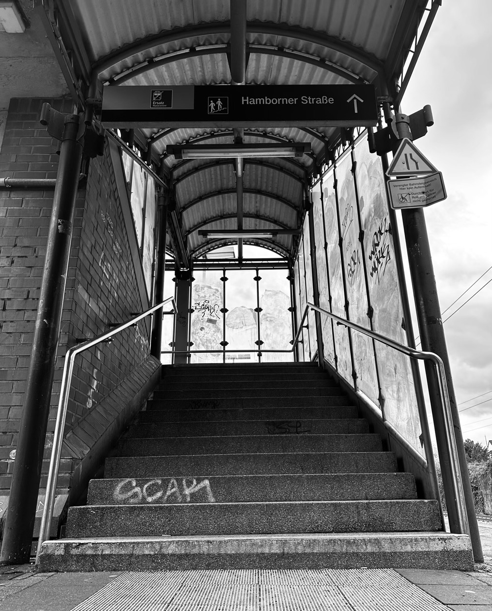 Black and white photo of a stone stair well, going up, at a train station.