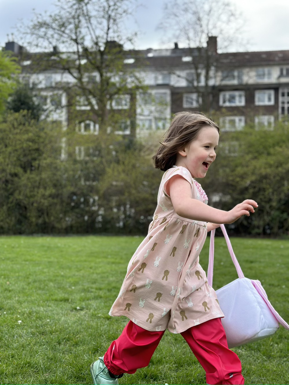 Little girl laughing while running through a park carrying an Easter basket hunting for eggs.