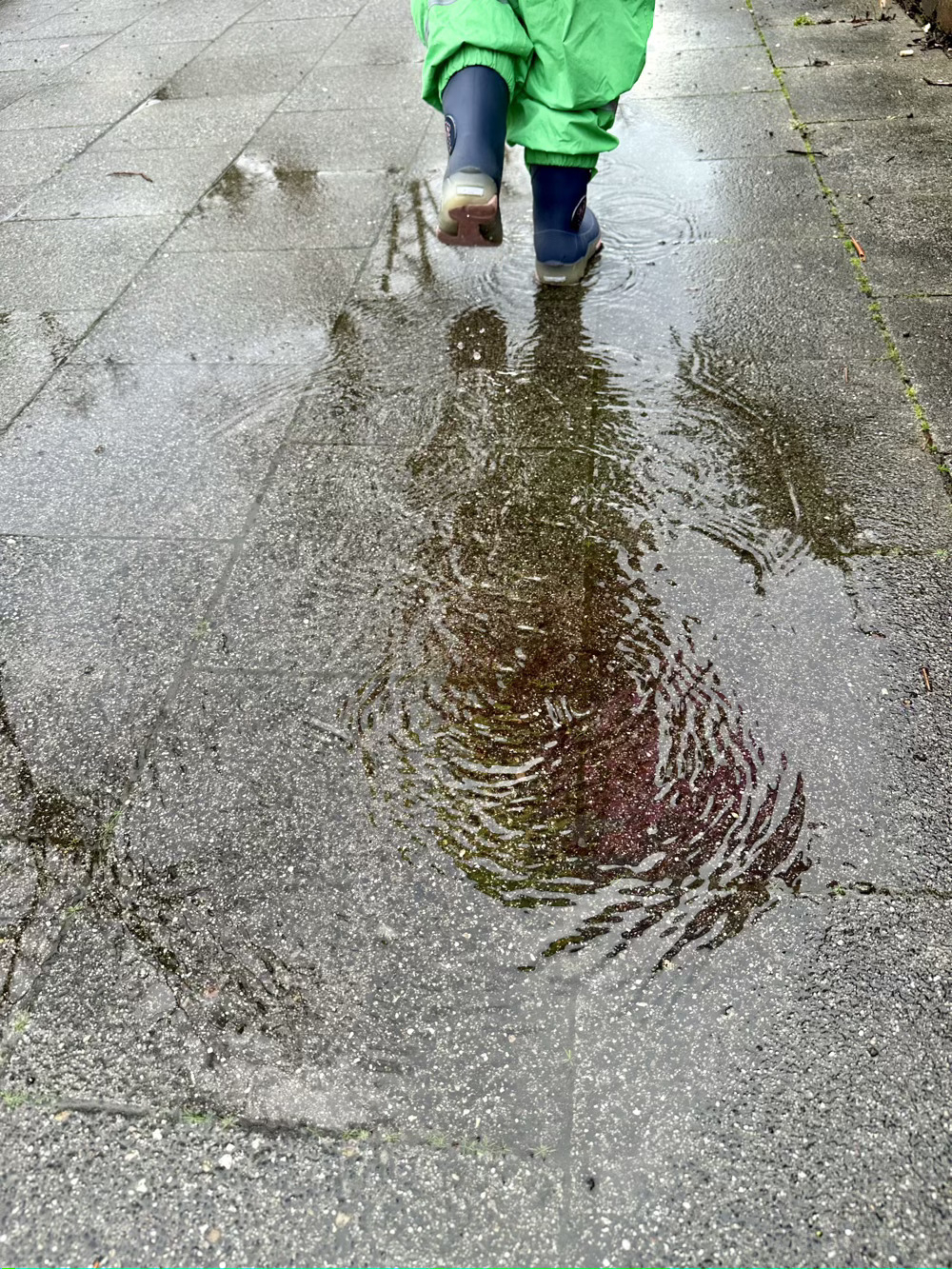 Reflection in puddle on the sidewalk of little girl walking away.