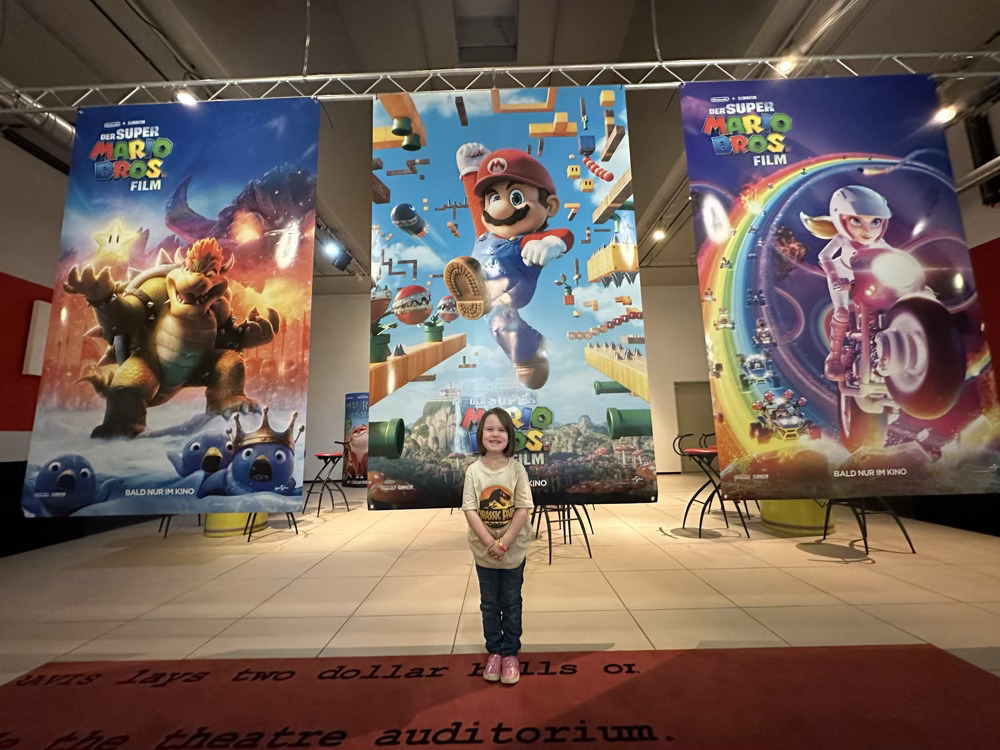 Little girl standing in front of three big Super Mario movie posters.