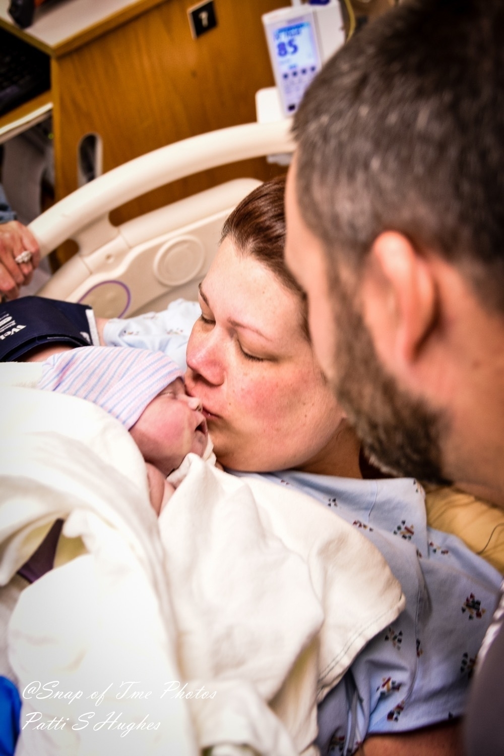 Mother, lying in hospital bed, kissing newborn baby, right after birth.