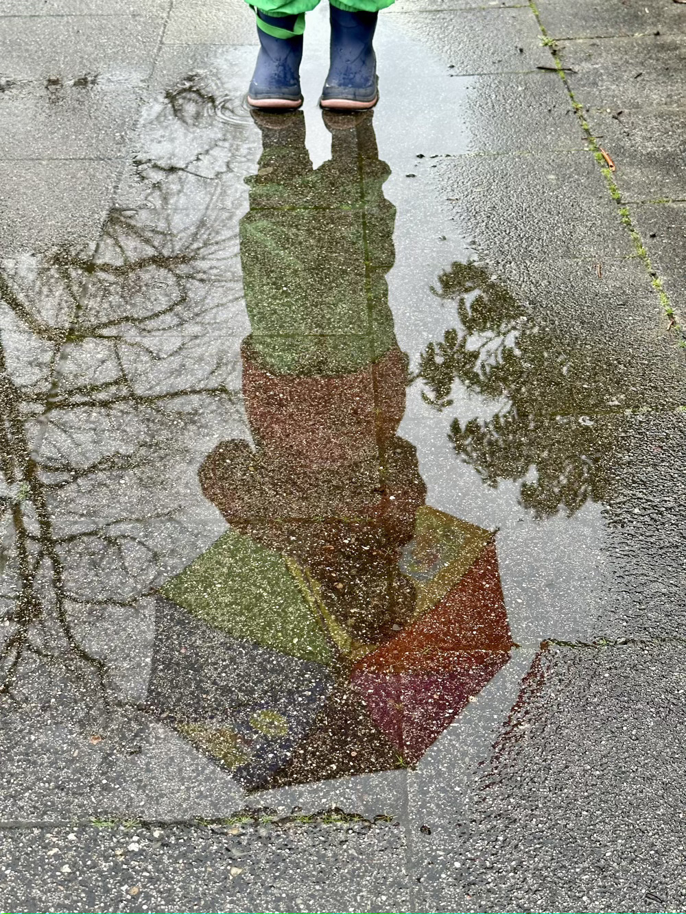 Reflection of little girl standing with an umbrella in a puddle on a sidewalk.