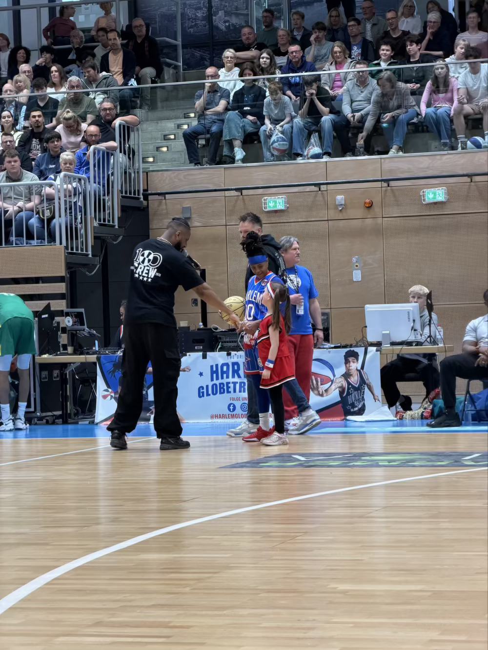 Watching a basketball game from court-side. Little girl being welcomed onto the court with one of the players during game time for a special trick. 