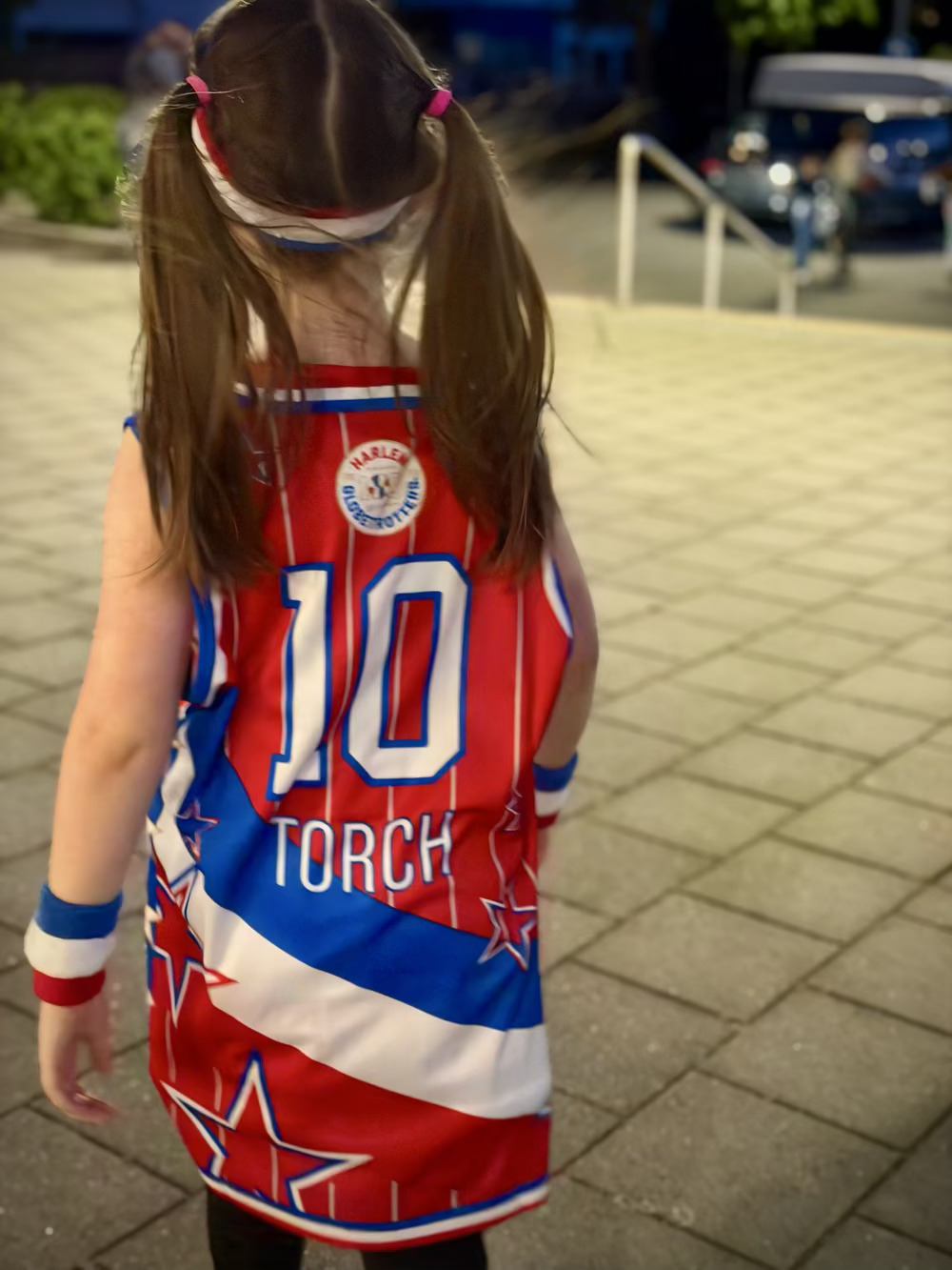 Little girl walking away wearing a Harlem Globetrotters jersey. With the name Torch on the back. 