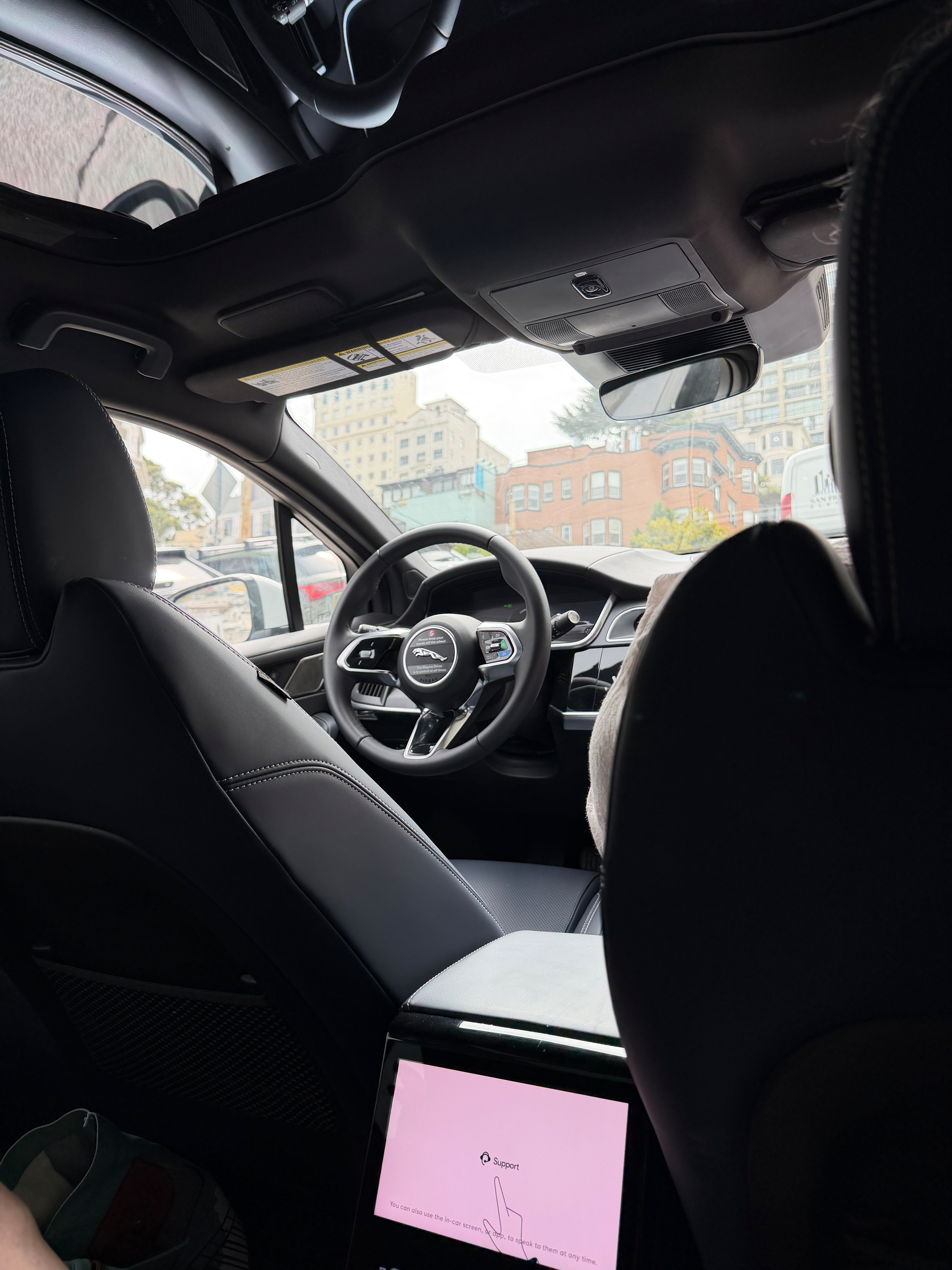 Interior view of a Waymo car. Sitting in the backseat, passenger side, facing toward the driver seat.