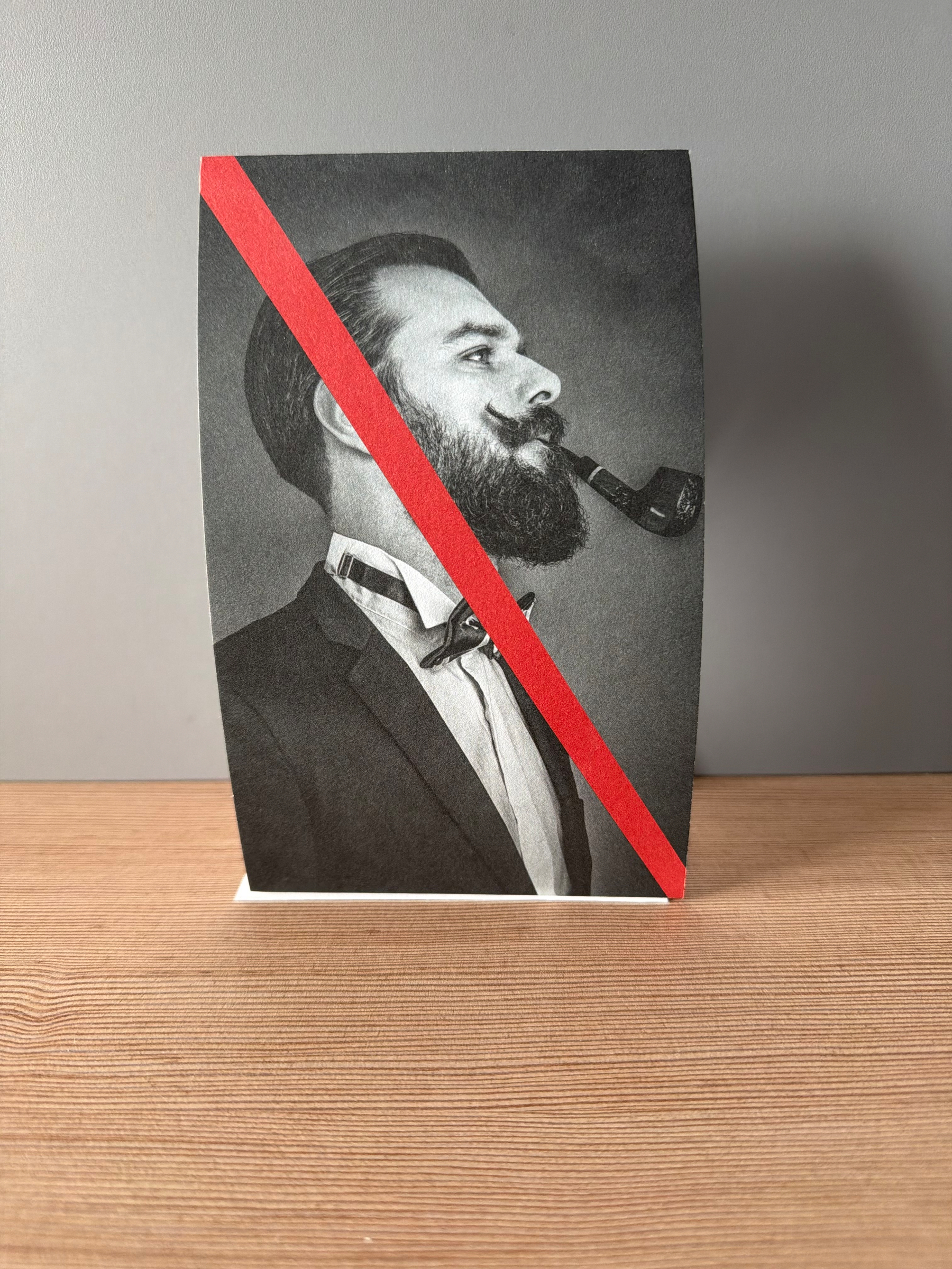 Black and white photo propped up on a table. The photo is of a man smoking a pipe with a red line across the photo from the t