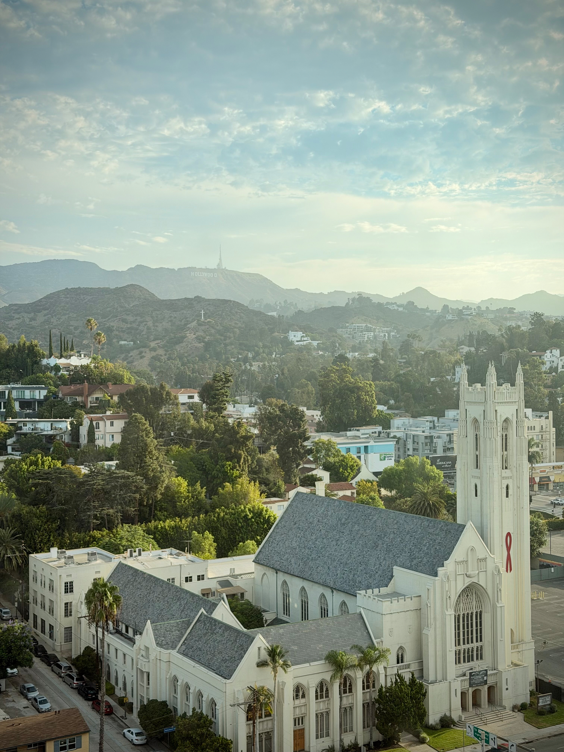 Picture of a church, in the foreground, surrounded by houses, with the Hollywood sign visible on the hills behind it.