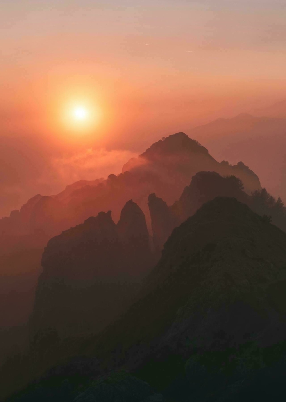 A tranquil sunrise illuminates misty mountainous peaks, creating a serene and majestic landscape.