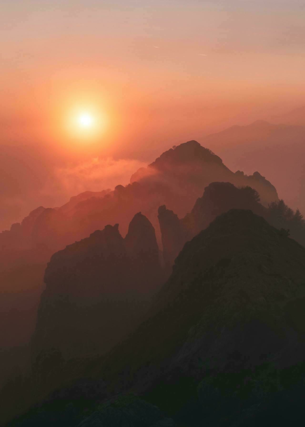 Auto-generated description: A tranquil sunrise illuminates misty mountainous peaks, creating a serene and majestic landscape.