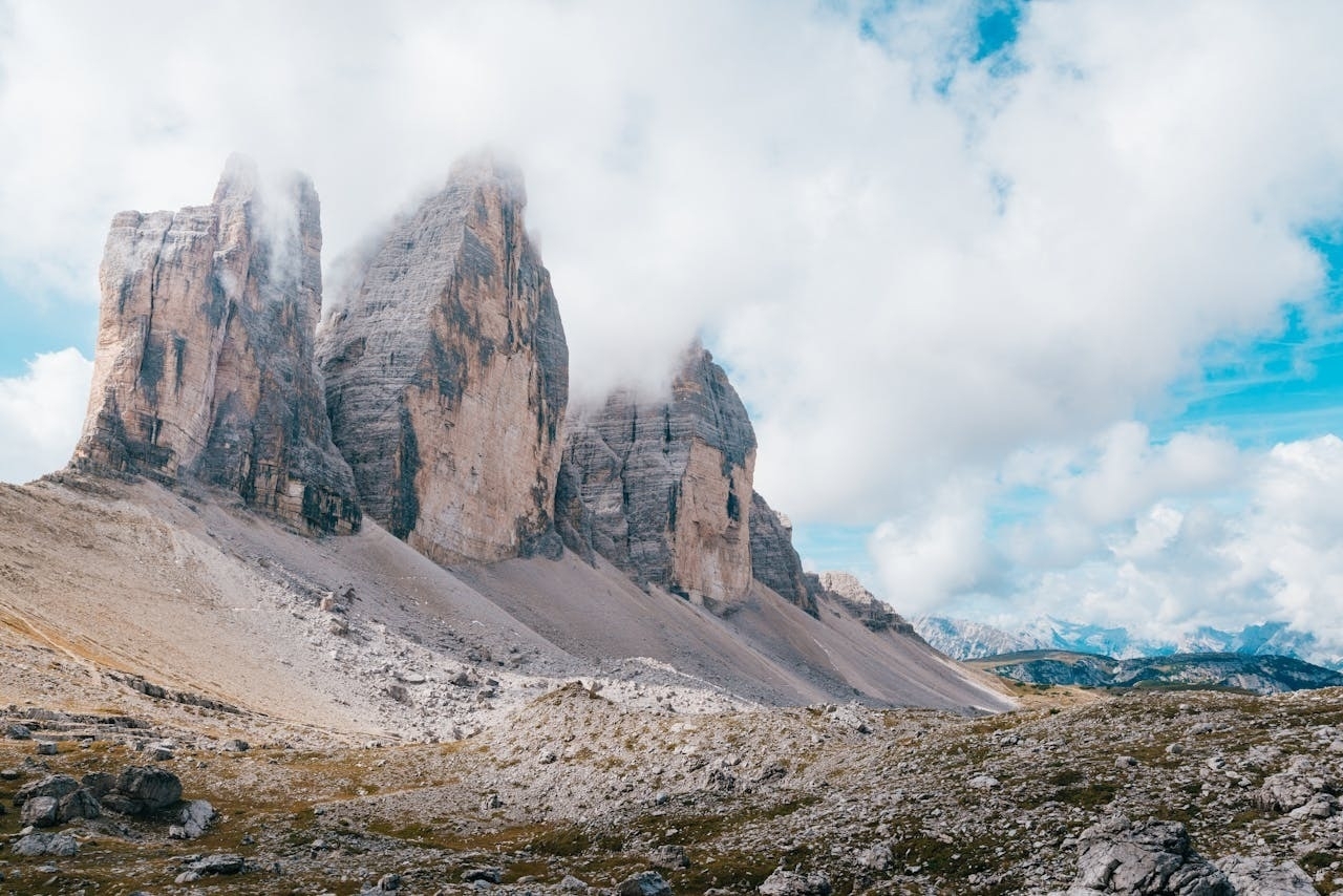 Auto-generated description: Three towering rock formations rise prominently amidst a landscape of rolling hills and a partly cloudy sky.