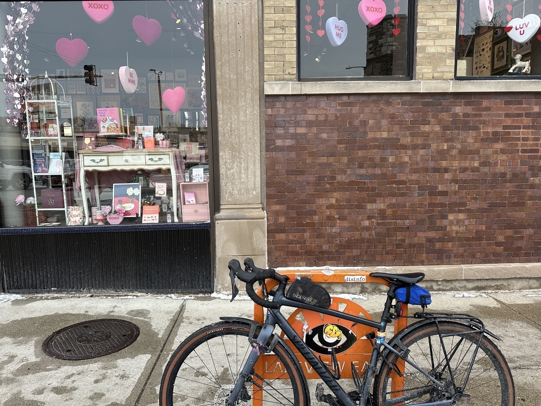 A bicycle is parked in front of a shop window decorated with pink heart-themed ornaments and signs.