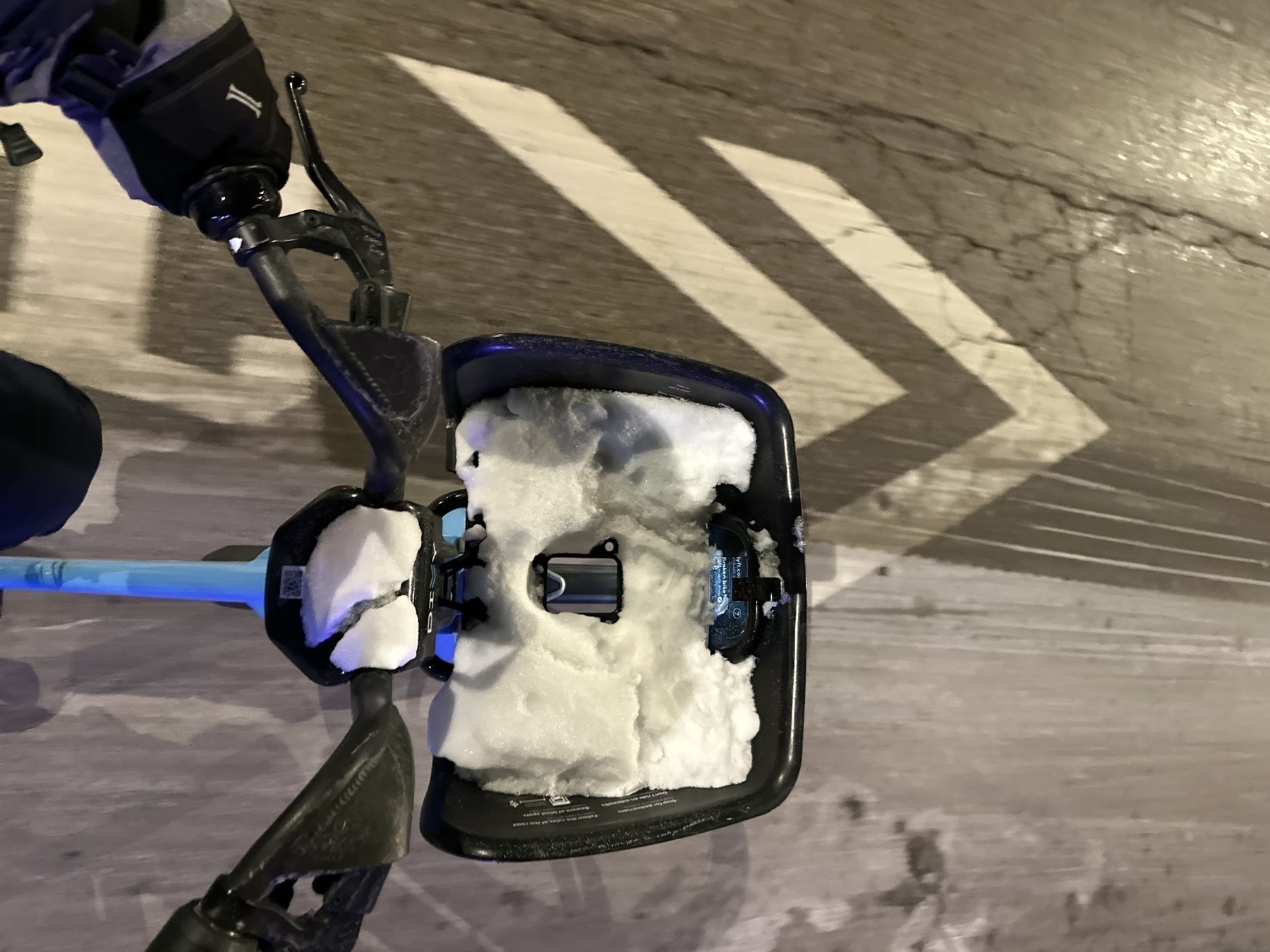 A close cropped photo, shot from above, of the front of a divvy in motion with a basket full of snow passing over a sharrow on a salted street.