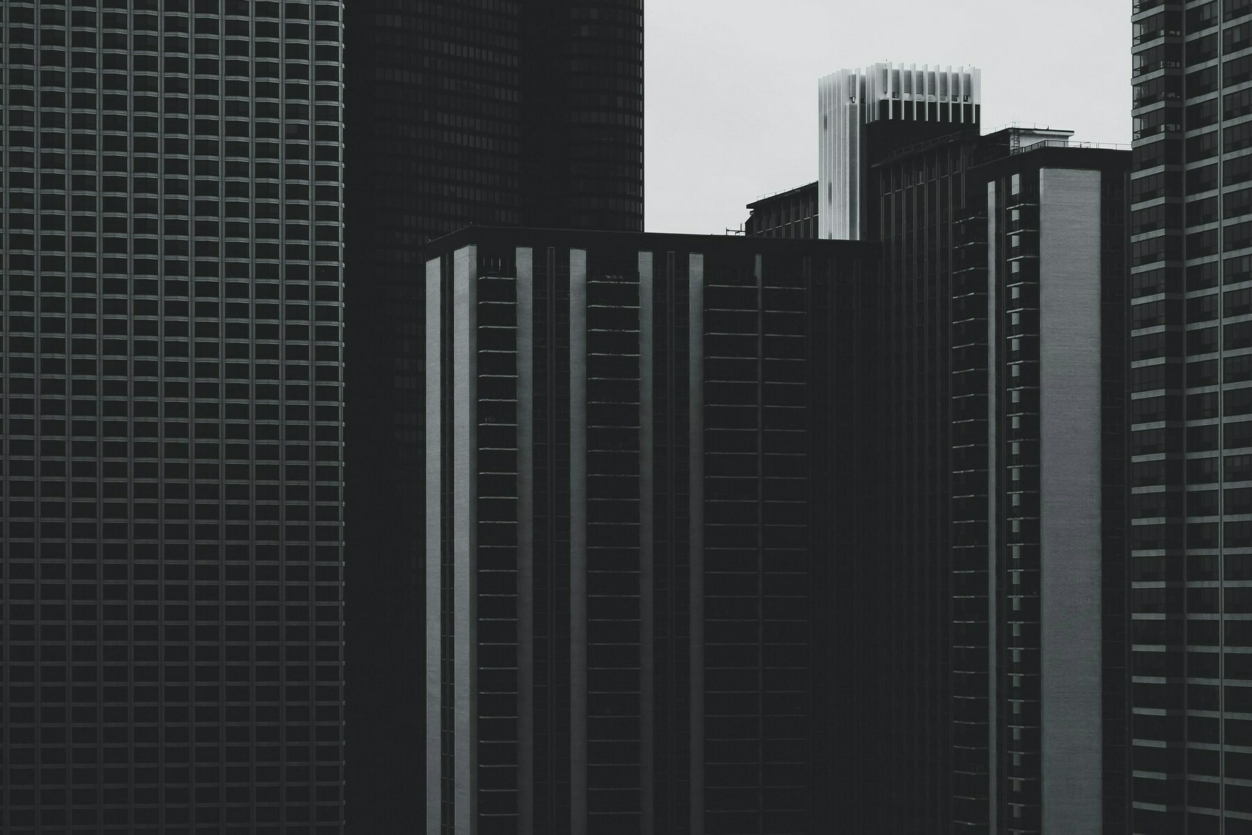 A cluster of tall, modern skyscrapers with geometric patterns and dark tones dominates the urban landscape.