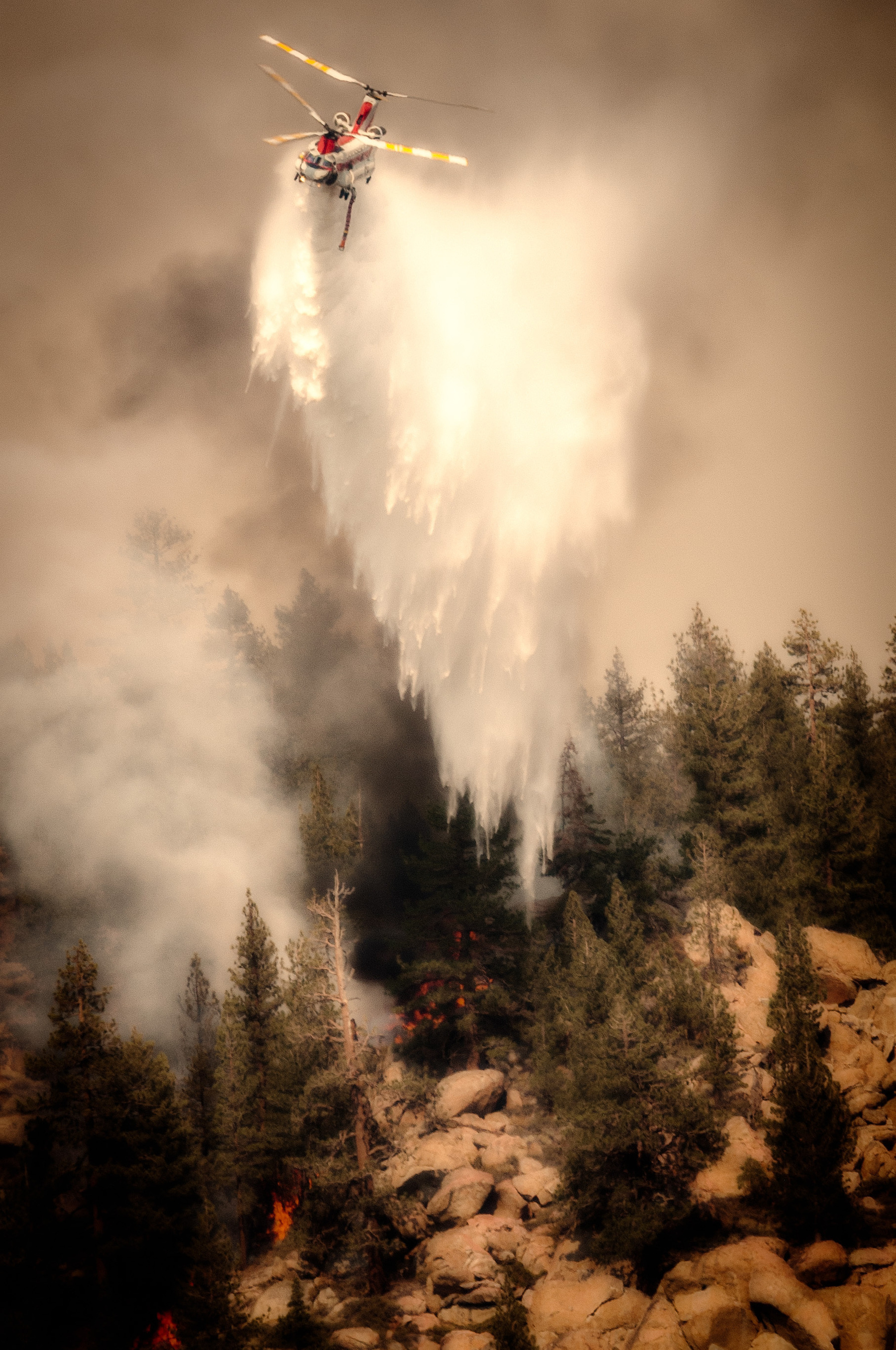 Auto-generated description: A helicopter drops water over a forest fire to extinguish the flames.