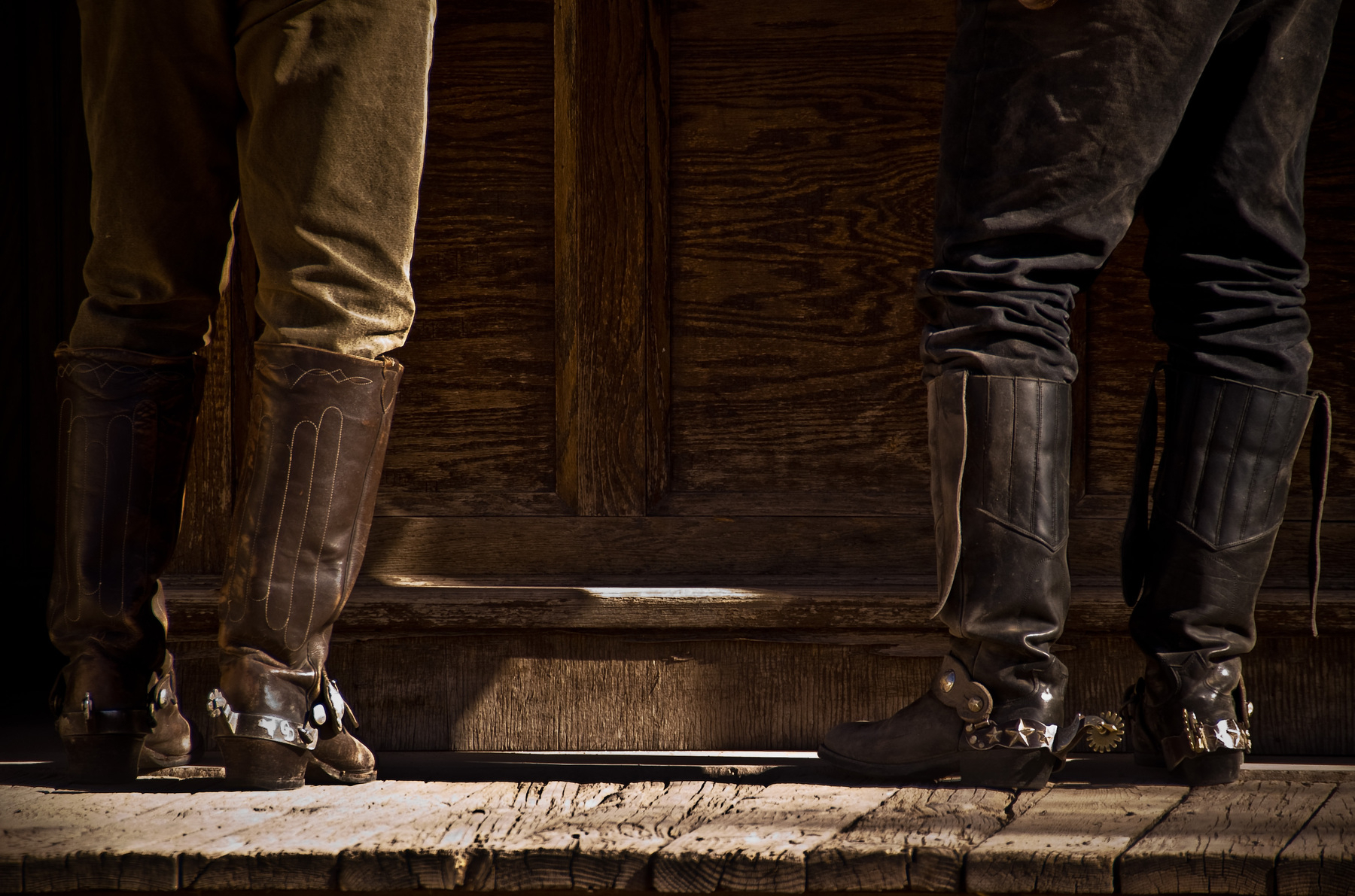 Auto-generated description: Two people standing on a wooden floor are wearing cowboy boots with spurs.