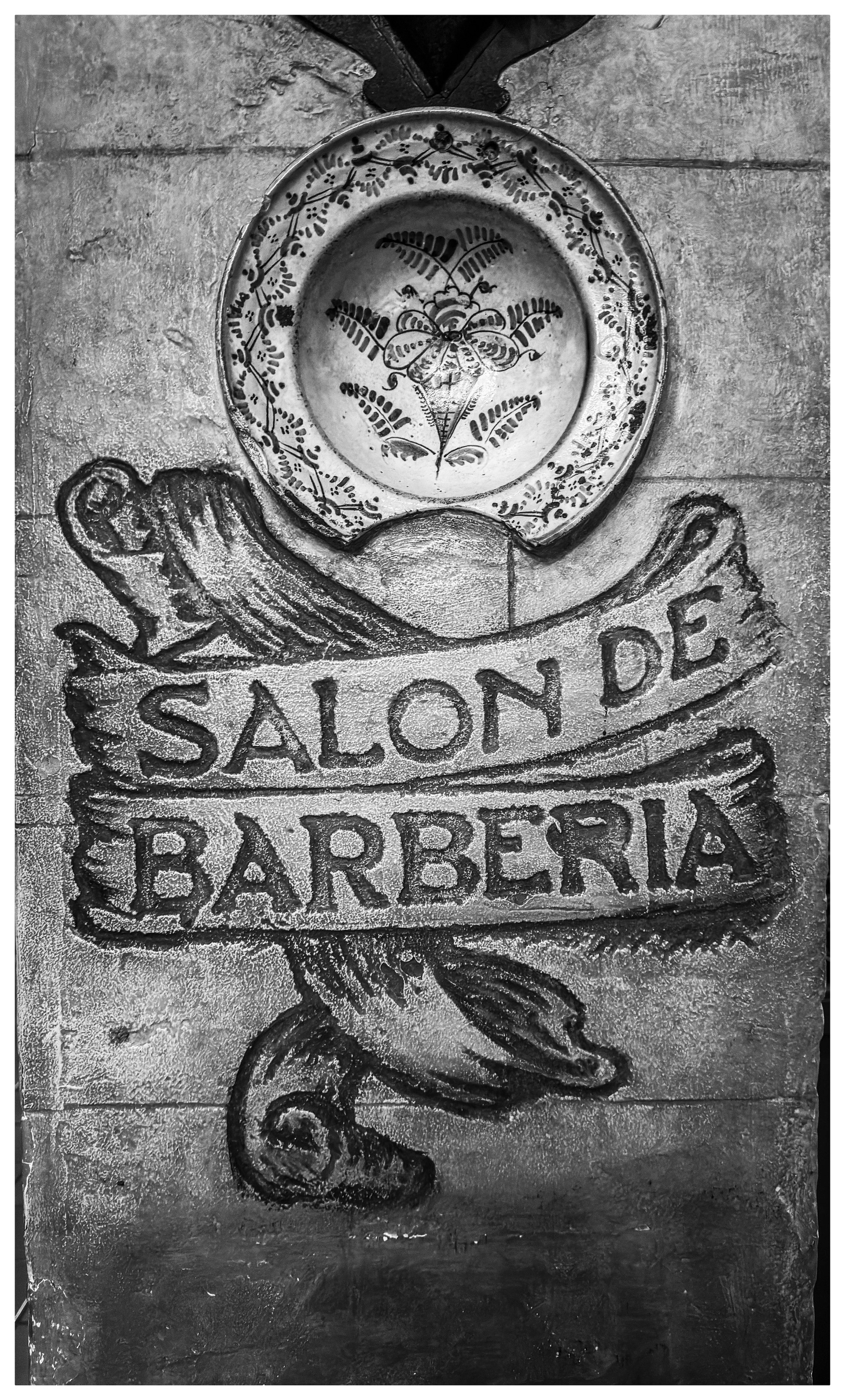 Auto-generated description: A plate with a floral design hangs above a wall painted with the text SALON DE BARBERIA.