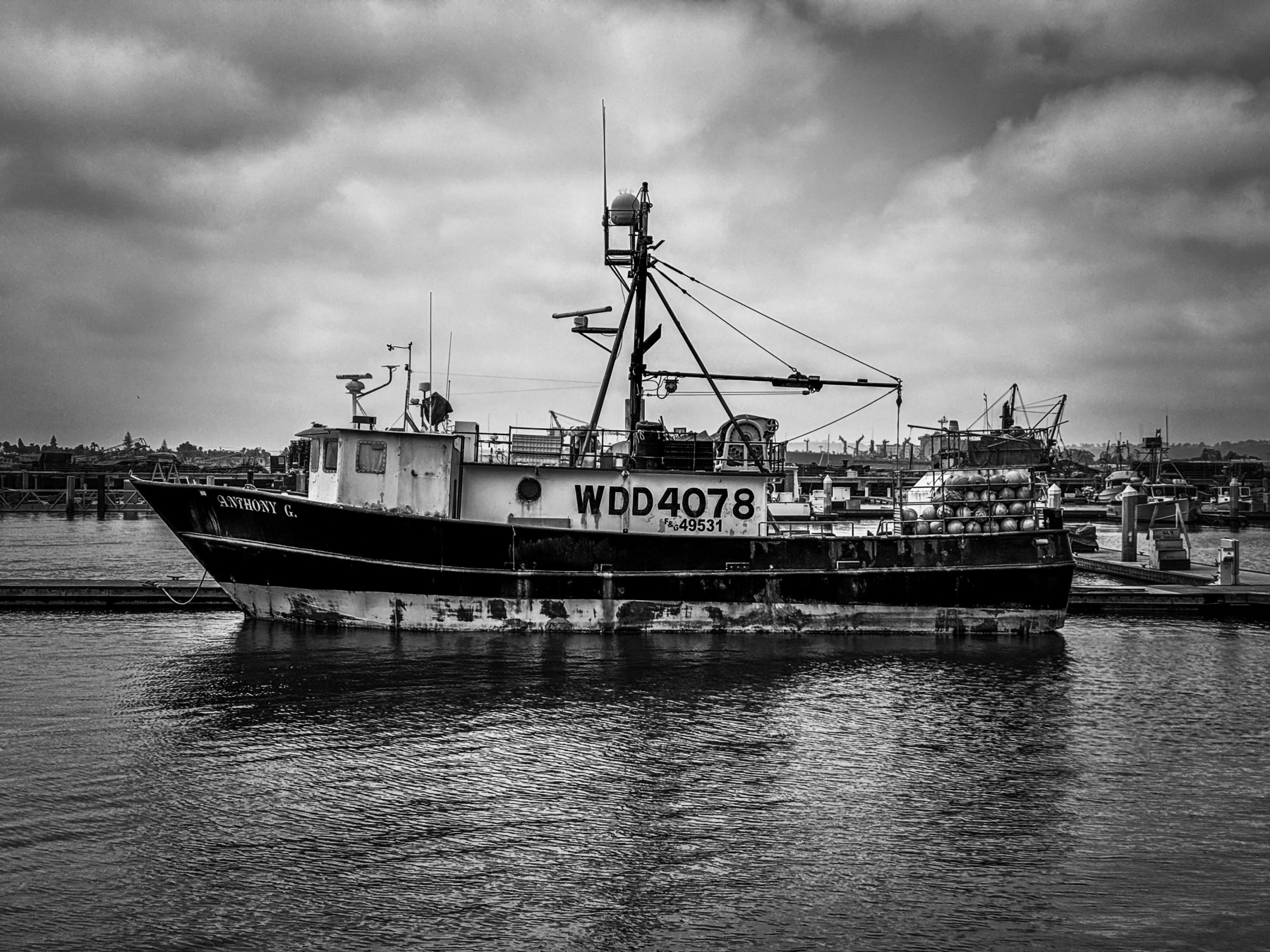 Auto-generated description: A black and white photograph of a fishing boat docked at a harbor under a cloudy sky.