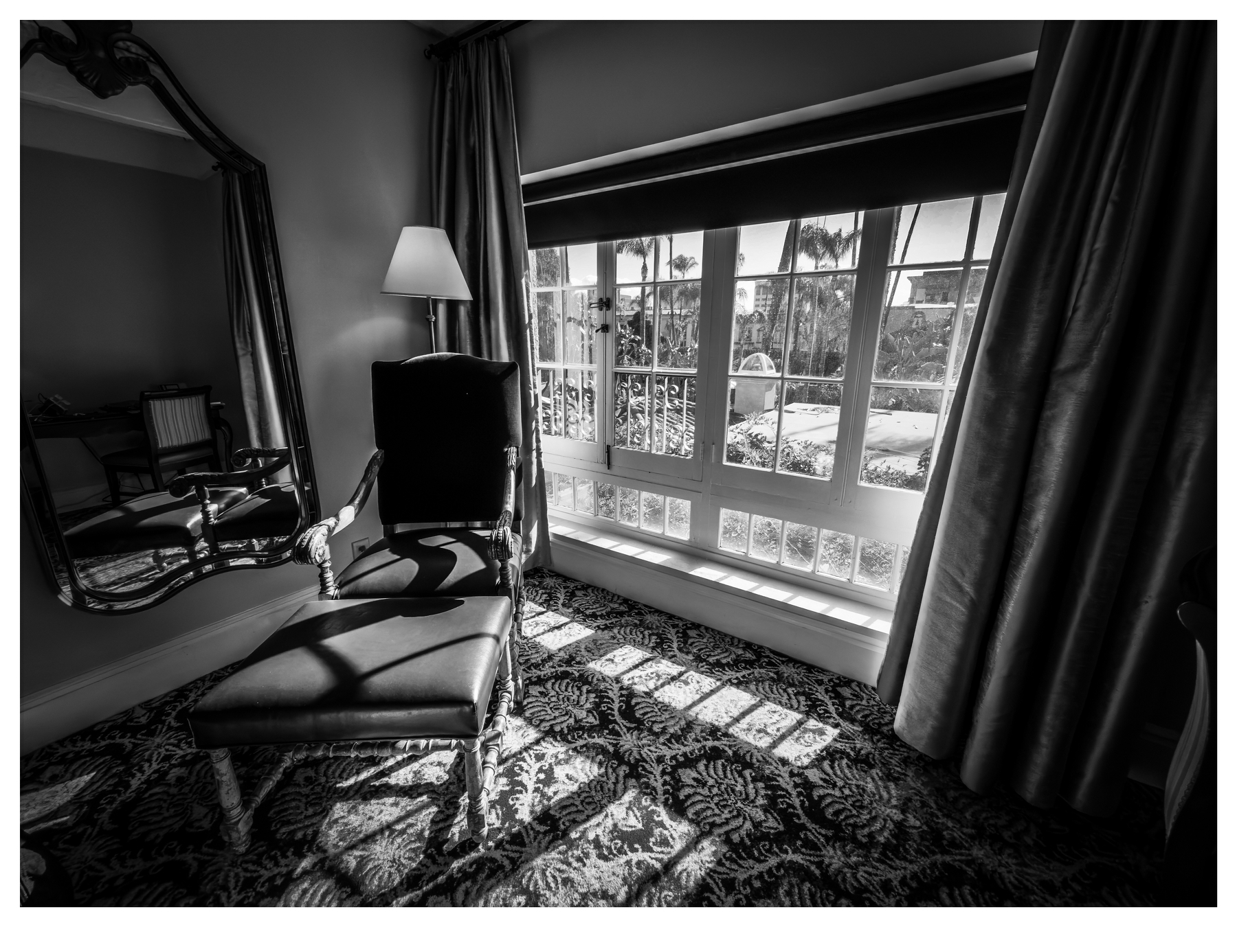 Auto-generated description: A sophisticated room features an upholstered chair and ottoman near a large window, adorned with patterned carpeting and elegant drapery, capturing light and shadows beautifully.