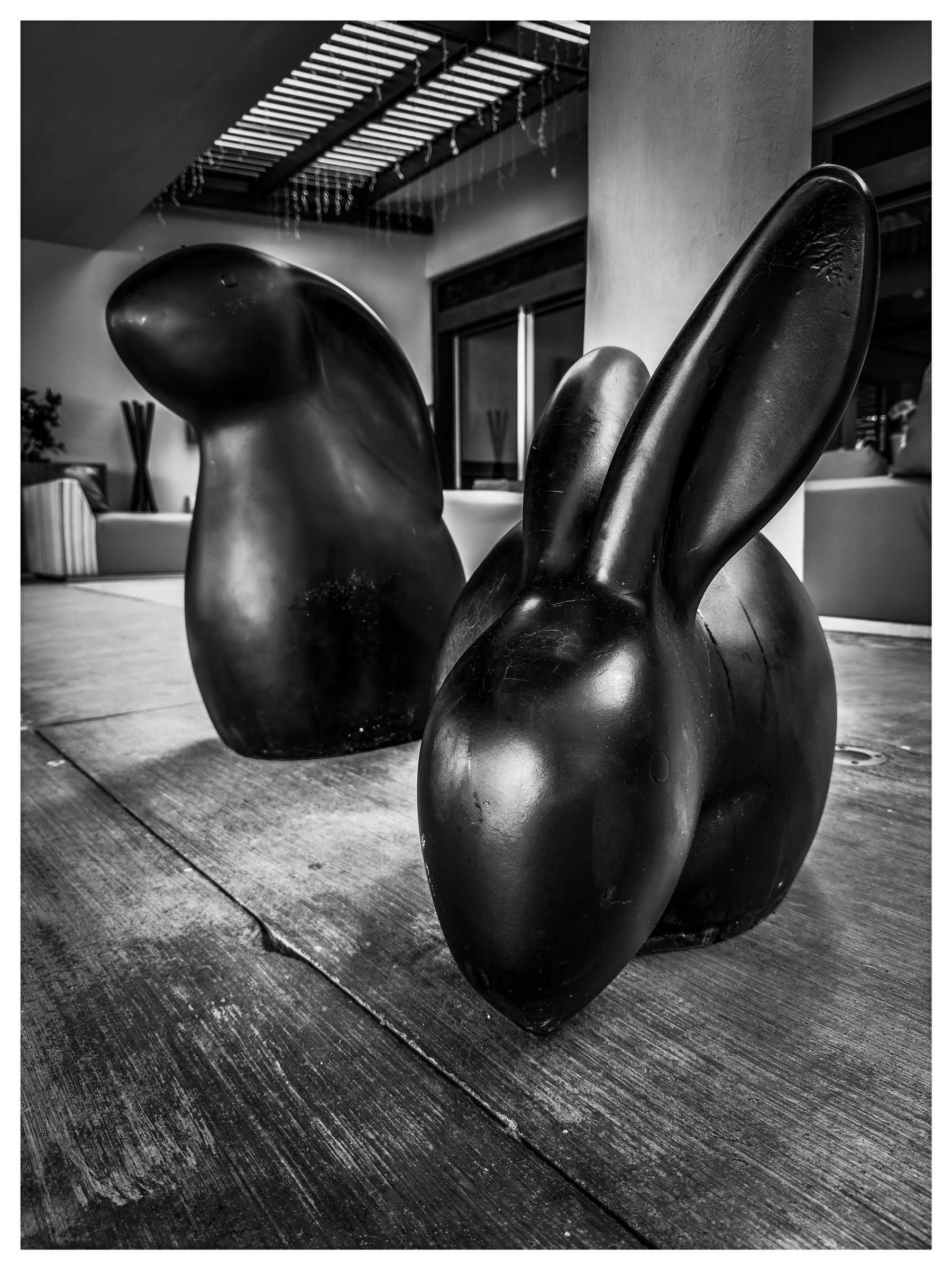 Auto-generated description: Two abstract, glossy sculptures, resembling a rabbit and another animal, are positioned on a wooden floor in a modern indoor setting.