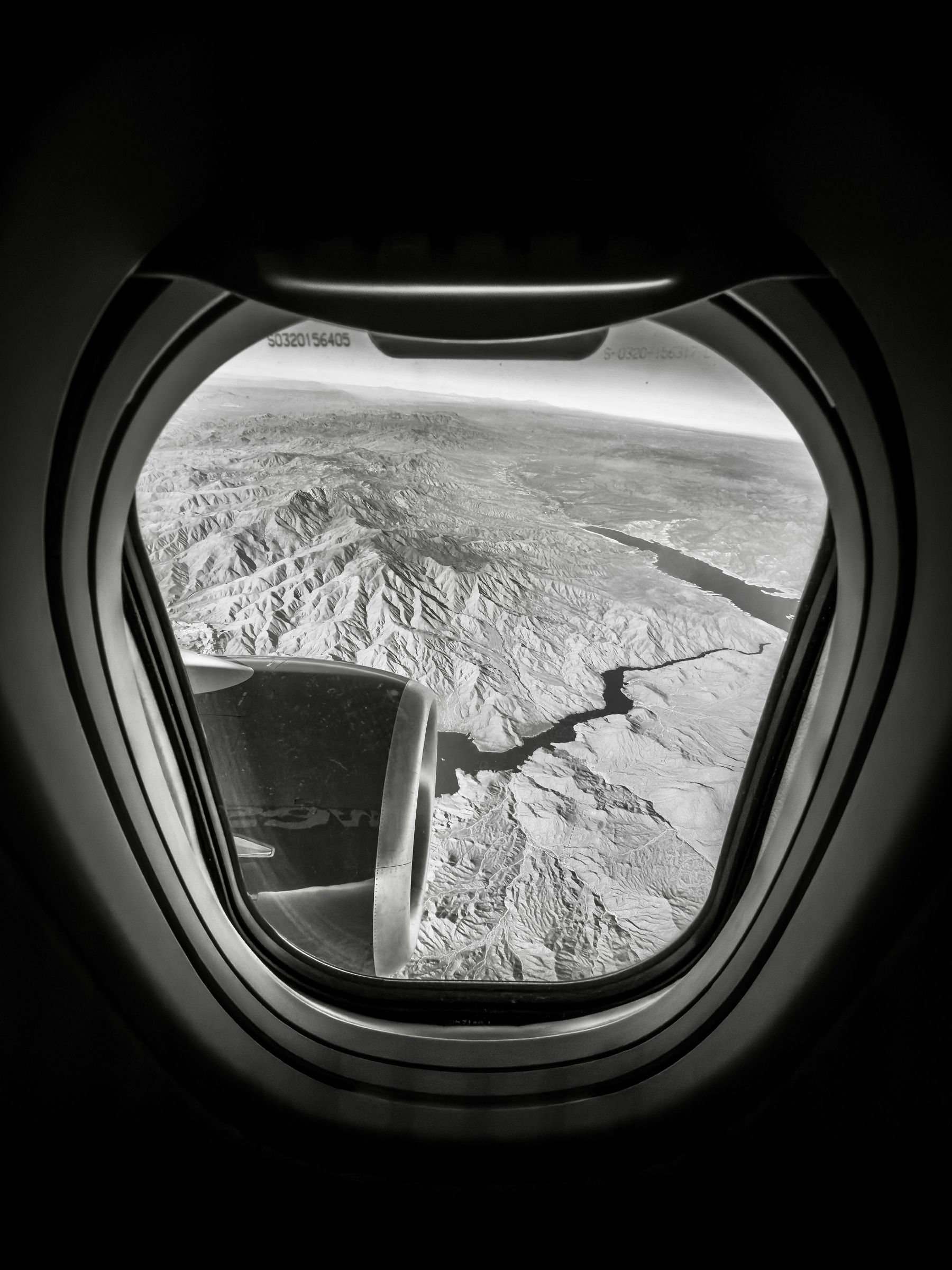 Auto-generated description: An aerial view through an airplane window shows mountainous terrain and a winding river below.