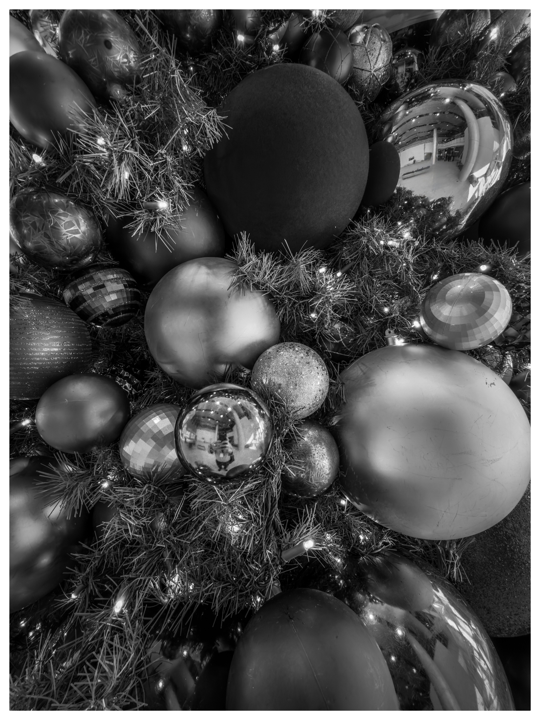 Auto-generated description: Various sizes of Christmas ornaments arranged with pine branches and lights create a festive and reflective display.