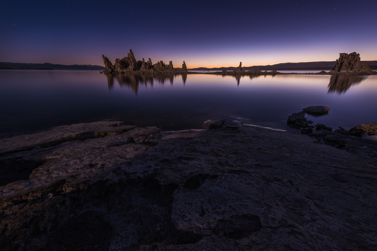 Auto-generated description: A serene twilight scene features tranquil waters with rocky formations silhouetted against a fading sunset.