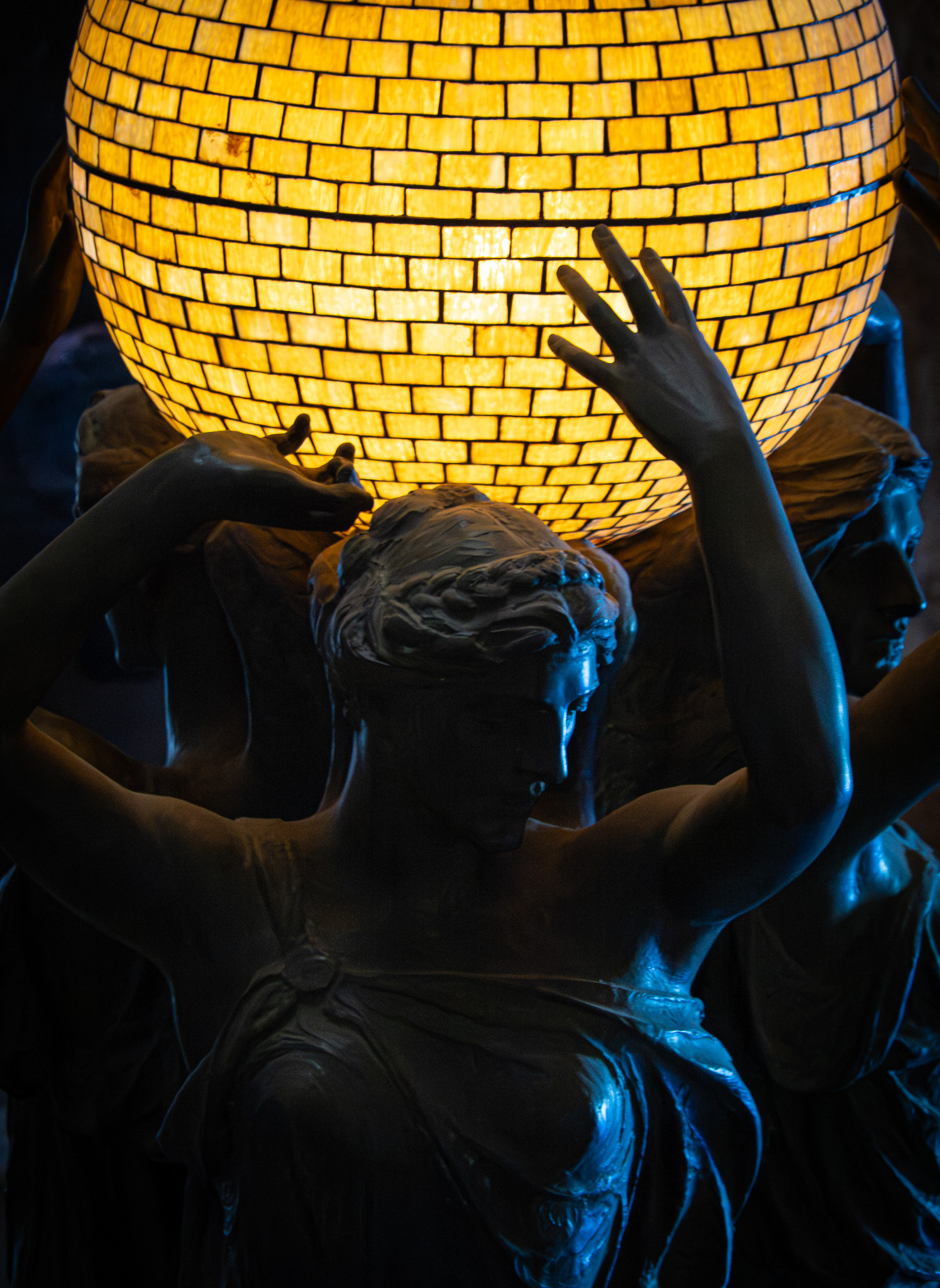 Auto-generated description: A statue of multiple figures holds up a large, glowing, yellow orb.