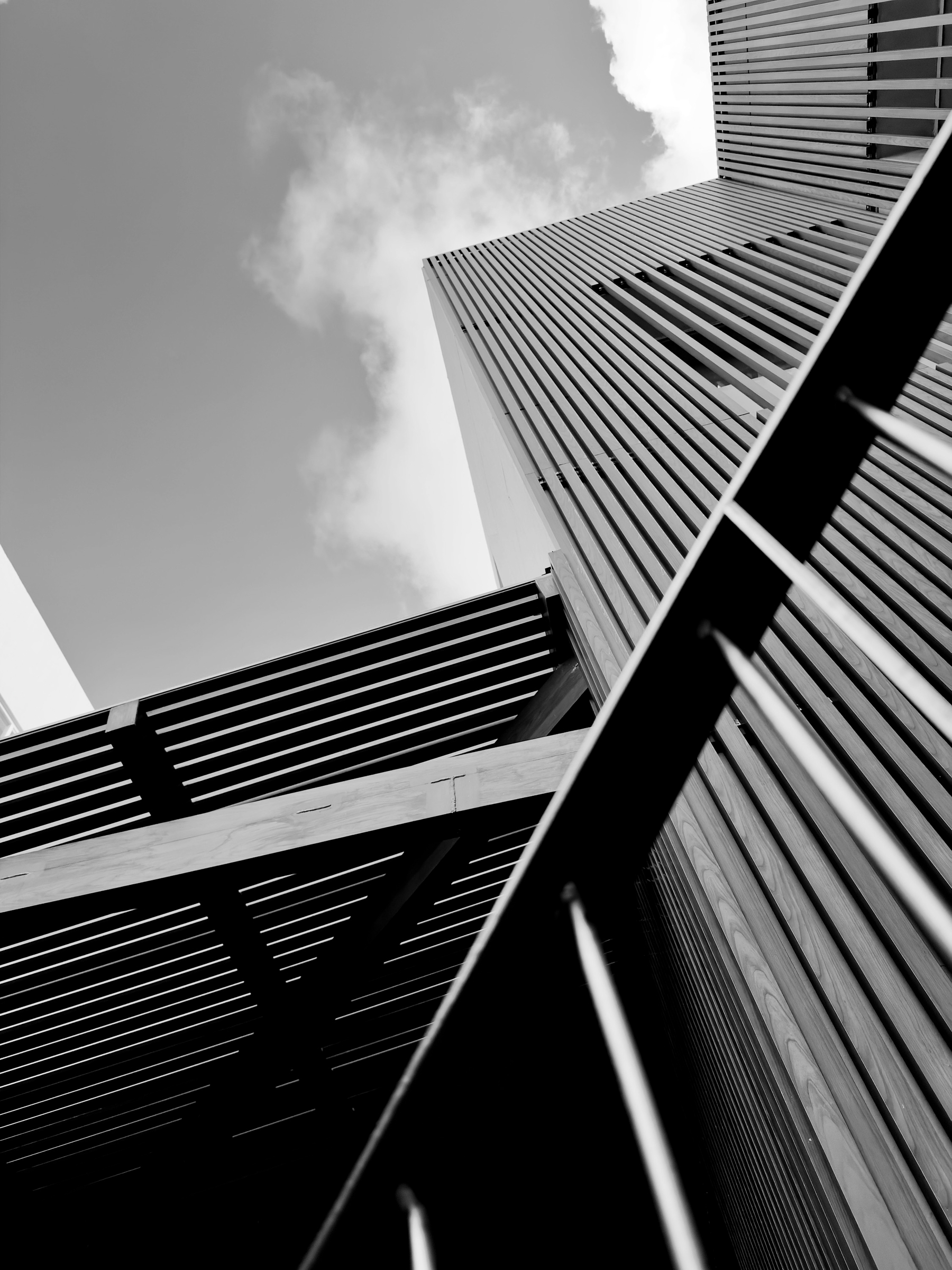 Auto-generated description: A black and white perspective shot of modern architectural structures with vertical and horizontal lines against a partly cloudy sky.