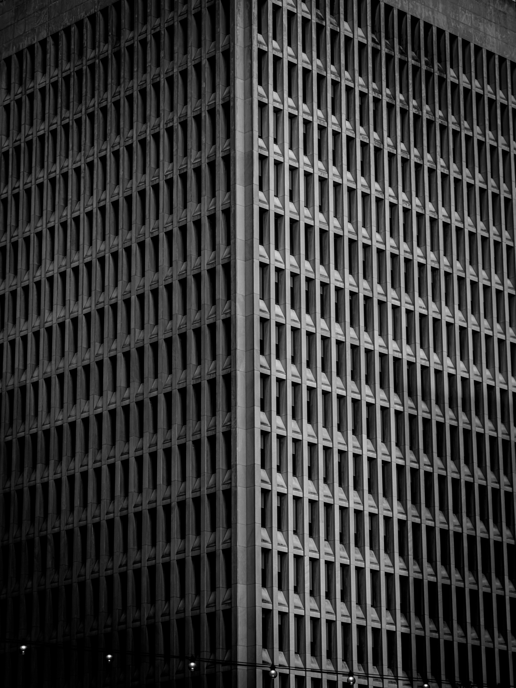 Auto-generated description: A tall building with a repetitive grid pattern of windows is shown in black and white, emphasizing its geometric architectural design.